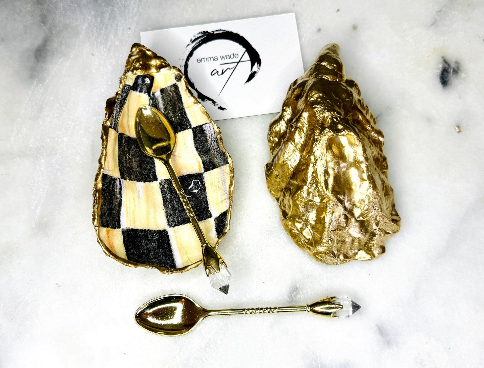 Handmade black, pearl and gold chequered oyster shell salt and pepper pinch pots, shown as a matching pair with small gold spoons on a light background. Natural Dorset shells decorated with a graphic pattern, gilded with gold leaf and sealed with a glossy, food-safe resin. Elegant coastal table decor and a unique gift for weddings, anniversaries or stylish dining tables, each piece one of a kind.