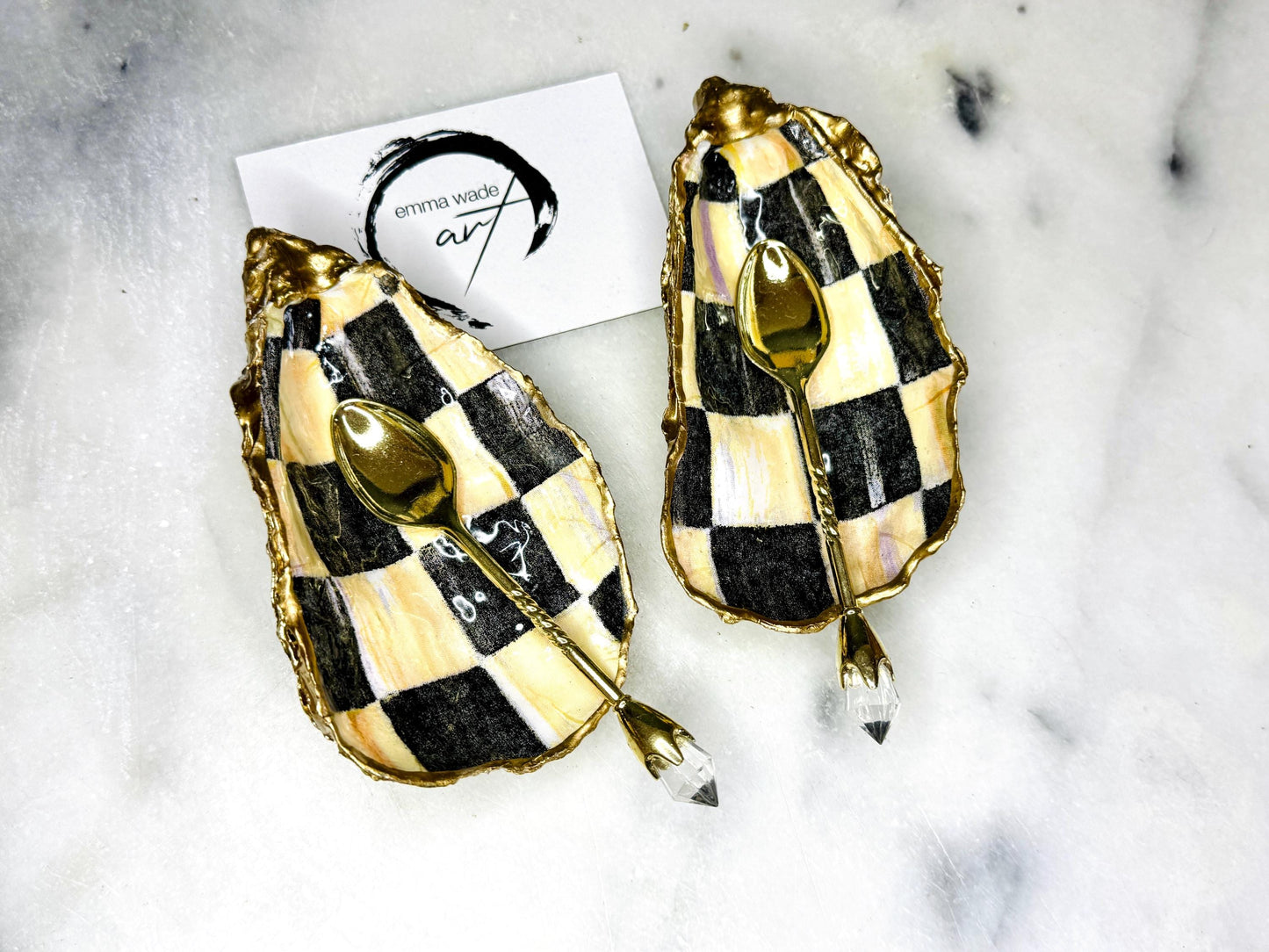 Handmade black, pearl and gold chequered oyster shell salt and pepper pinch pots, shown as a matching pair with small gold spoons on a light background. Natural Dorset shells decorated with a graphic pattern, gilded with gold leaf and sealed with a glossy, food-safe resin. Elegant coastal table decor and a unique gift for weddings, anniversaries or stylish dining tables, each piece one of a kind.