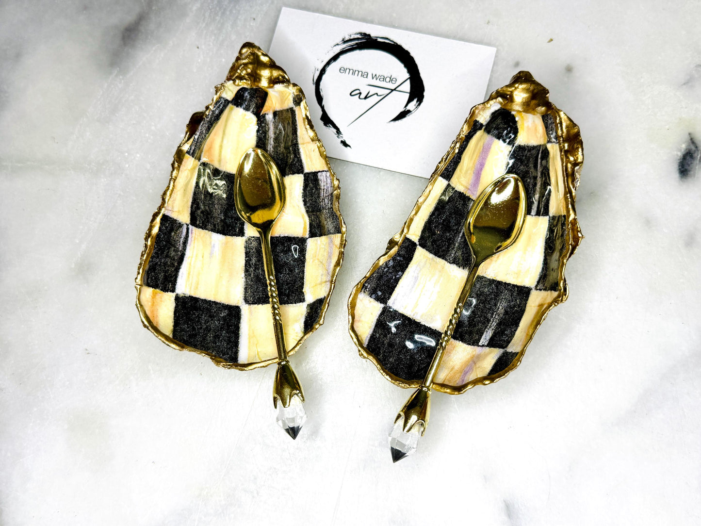 Handmade black, pearl and gold chequered oyster shell salt and pepper pinch pots, shown as a matching pair with small gold spoons on a light background. Natural Dorset shells decorated with a graphic pattern, gilded with gold leaf and sealed with a glossy, food-safe resin. Elegant coastal table decor and a unique gift for weddings, anniversaries or stylish dining tables, each piece one of a kind.