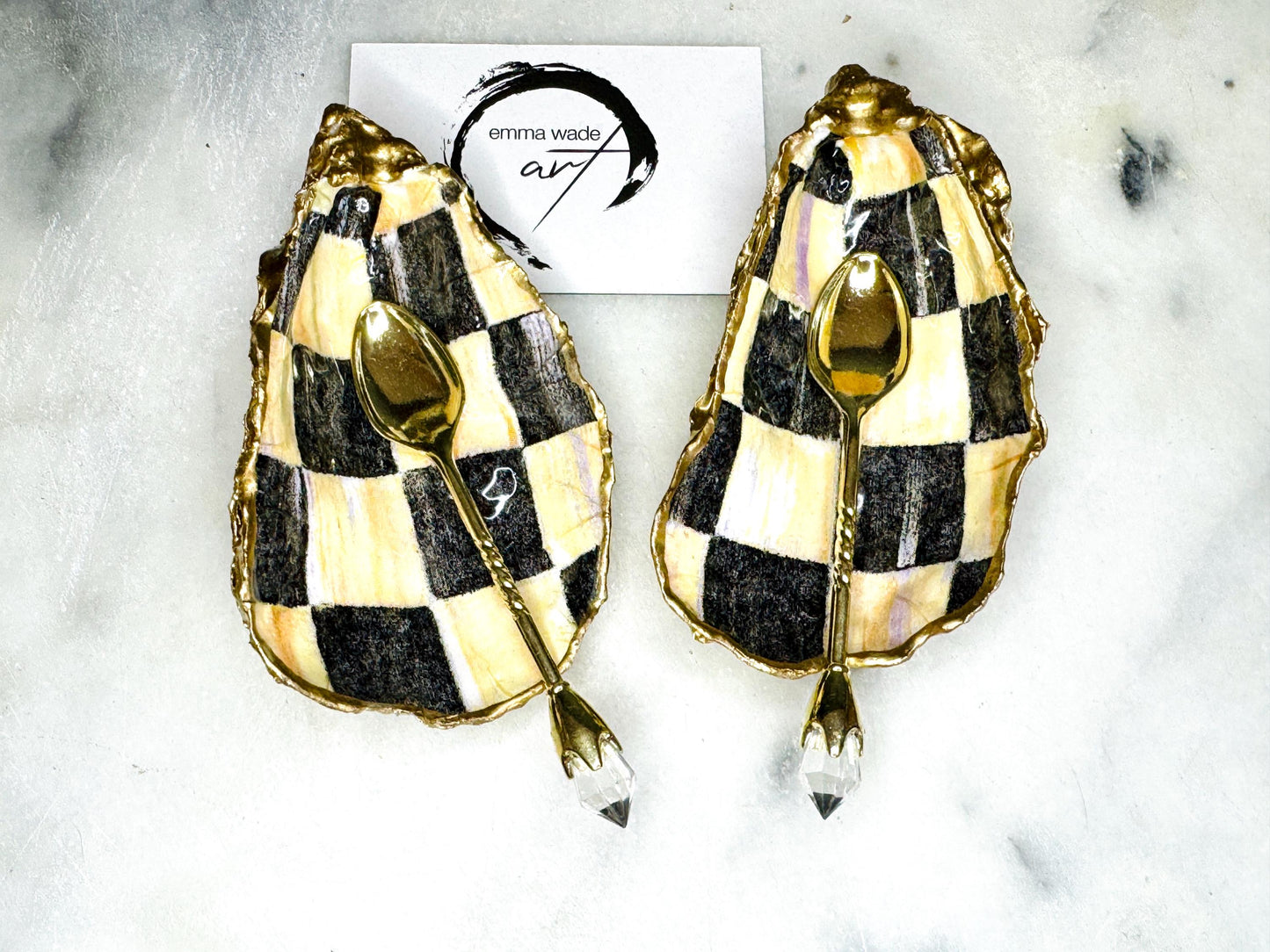 Handmade black, pearl and gold chequered oyster shell salt and pepper pinch pots, shown as a matching pair with small gold spoons on a light background. Natural Dorset shells decorated with a graphic pattern, gilded with gold leaf and sealed with a glossy, food-safe resin. Elegant coastal table decor and a unique gift for weddings, anniversaries or stylish dining tables, each piece one of a kind.