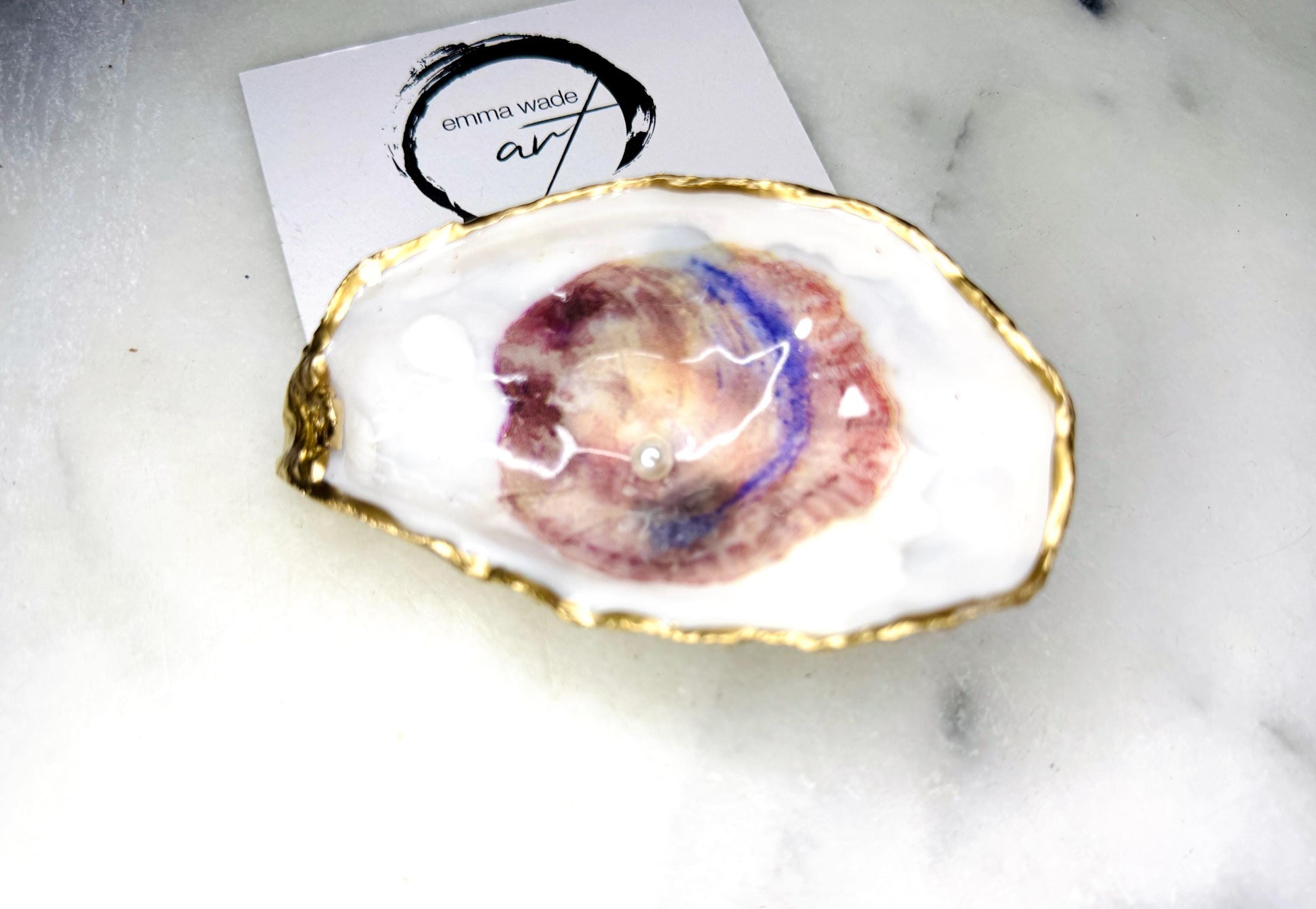 Handmade Dorset oyster shell trinket dish featuring a blue and beige watercolour oyster illustration with Swarovski pearl detail, finished with hand-applied gold leaf edging and glossy resin. Coastal-inspired jewellery dish and ring holder available in multiple sizes including XL oyster shells. Elegant handmade coastal décor gift ideal for weddings, birthdays, anniversaries, and luxury beach house interiors.