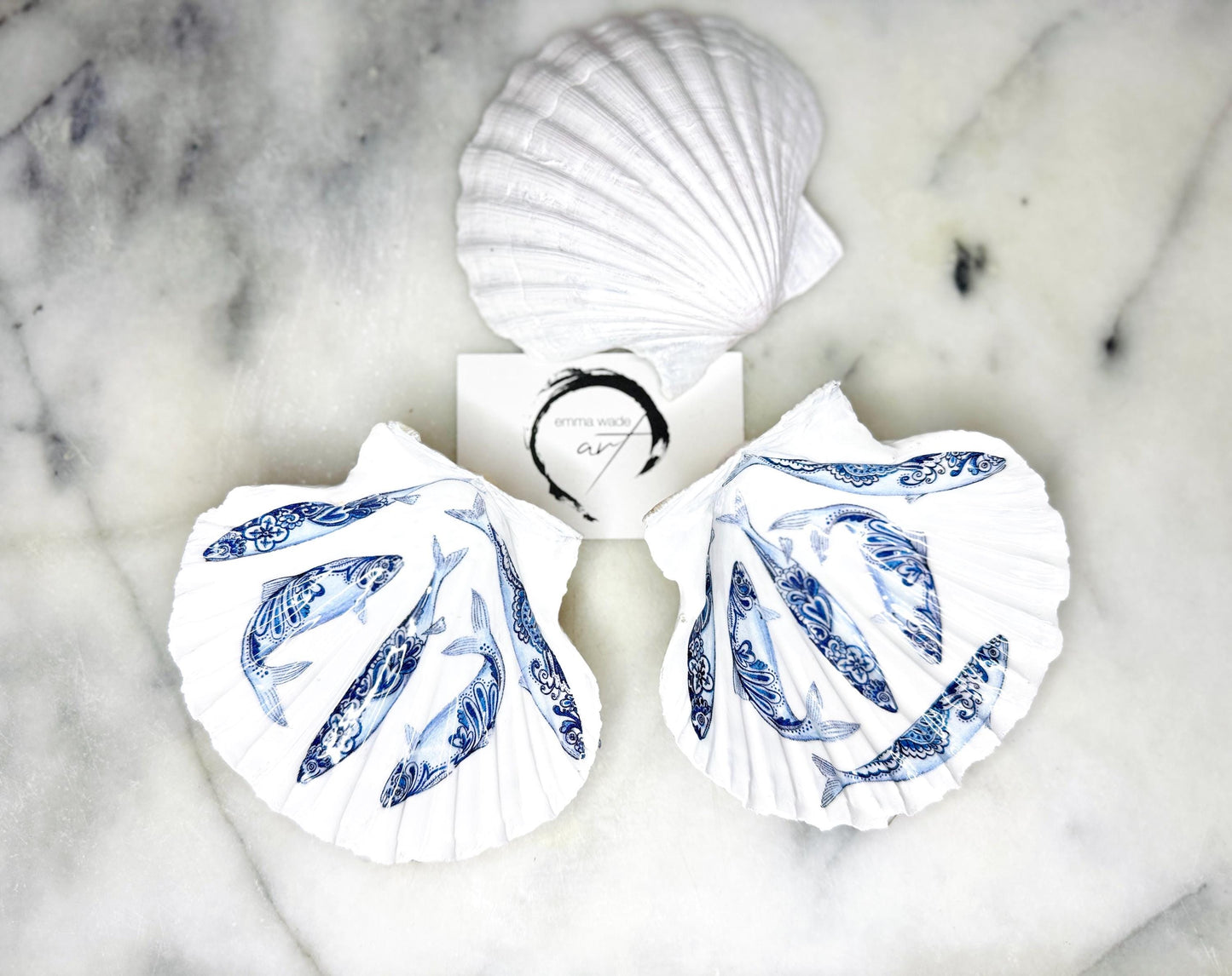 Handmade Dorset scallop shell trinket dishes featuring blue and white paisley fish illustrations with hand-painted gold leaf edging and glossy crystal clear resin. Coastal Scandinavian inspired jewellery dishes styled on a soft neutral background with elegant nautical fish artwork and luxurious gilded detailing.