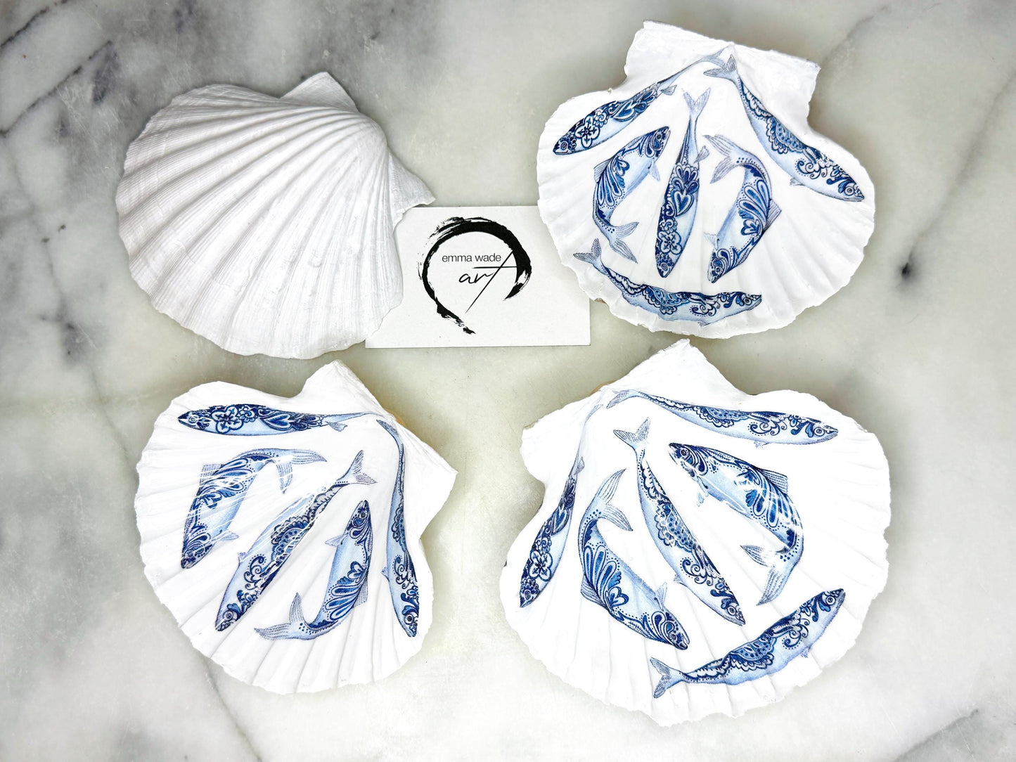 Handmade Dorset scallop shell trinket dishes featuring blue and white paisley fish illustrations with hand-painted gold leaf edging and glossy crystal clear resin. Coastal Scandinavian inspired jewellery dishes styled on a soft neutral background with elegant nautical fish artwork and luxurious gilded detailing.