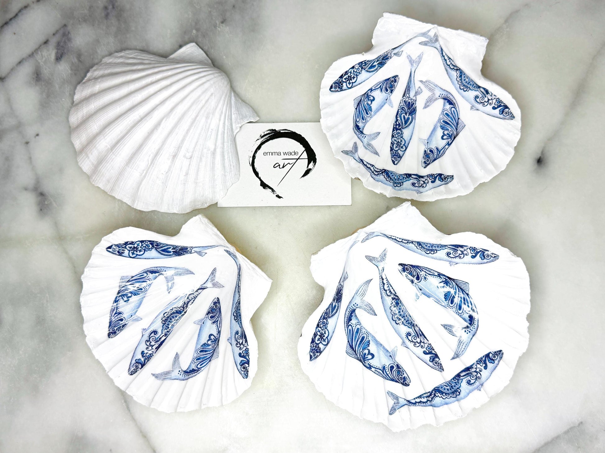 Handmade Dorset scallop shell trinket dishes featuring blue and white paisley fish illustrations with hand-painted gold leaf edging and glossy crystal clear resin. Coastal Scandinavian inspired jewellery dishes styled on a soft neutral background with elegant nautical fish artwork and luxurious gilded detailing.