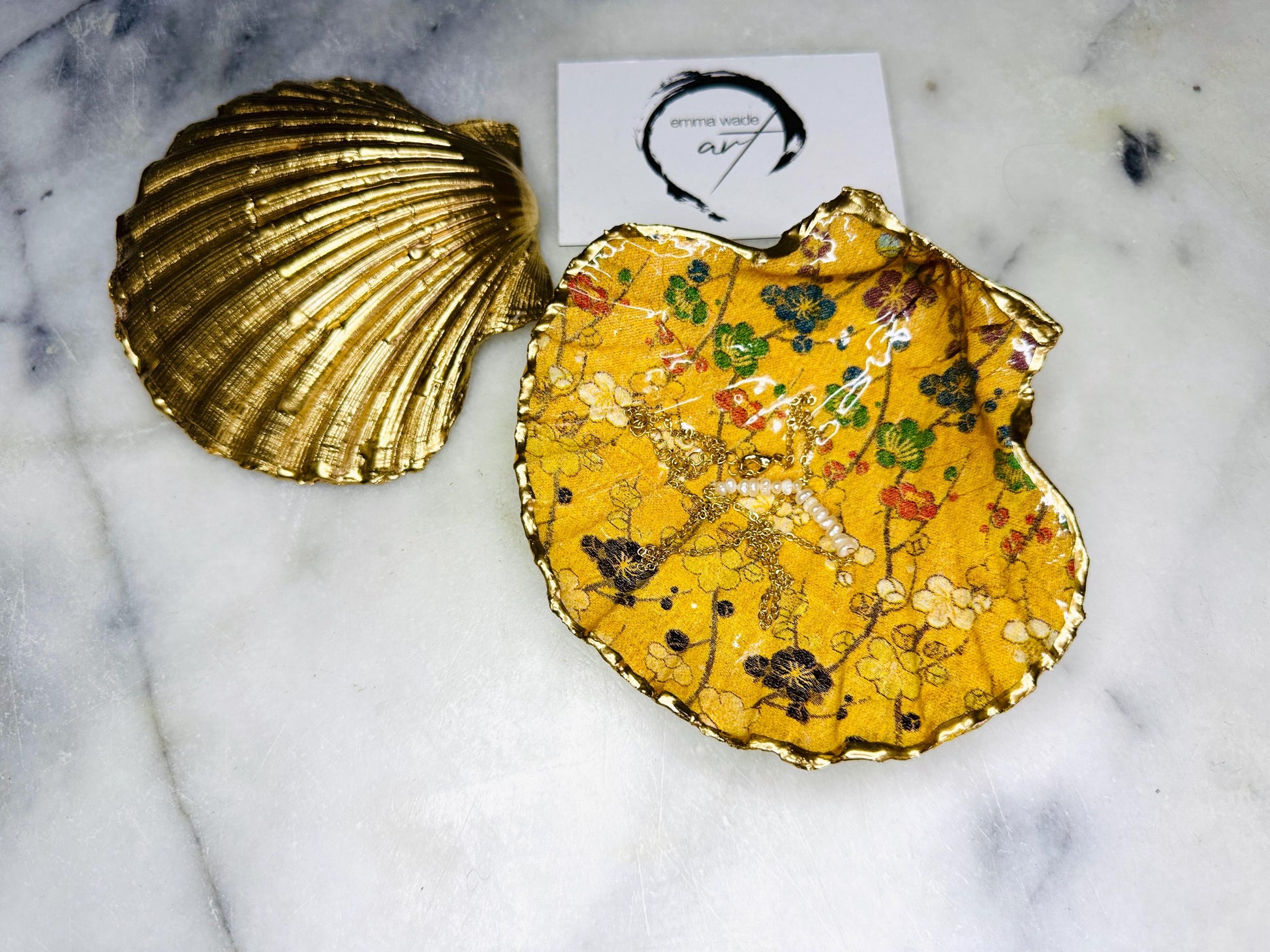 Handmade Dorset scallop shell trinket dish with Japanese plum blossom floral design on golden yellow background, finished with real liquid gold leaf edging and sealed in glossy resin. Unique coastal home decor piece, ideal as a jewellery dish, ring holder, or trinket tray. Sustainably sourced shell, artisan crafted in the UK, perfect gift for birthdays, weddings, anniversaries, or elegant dressing table styling.