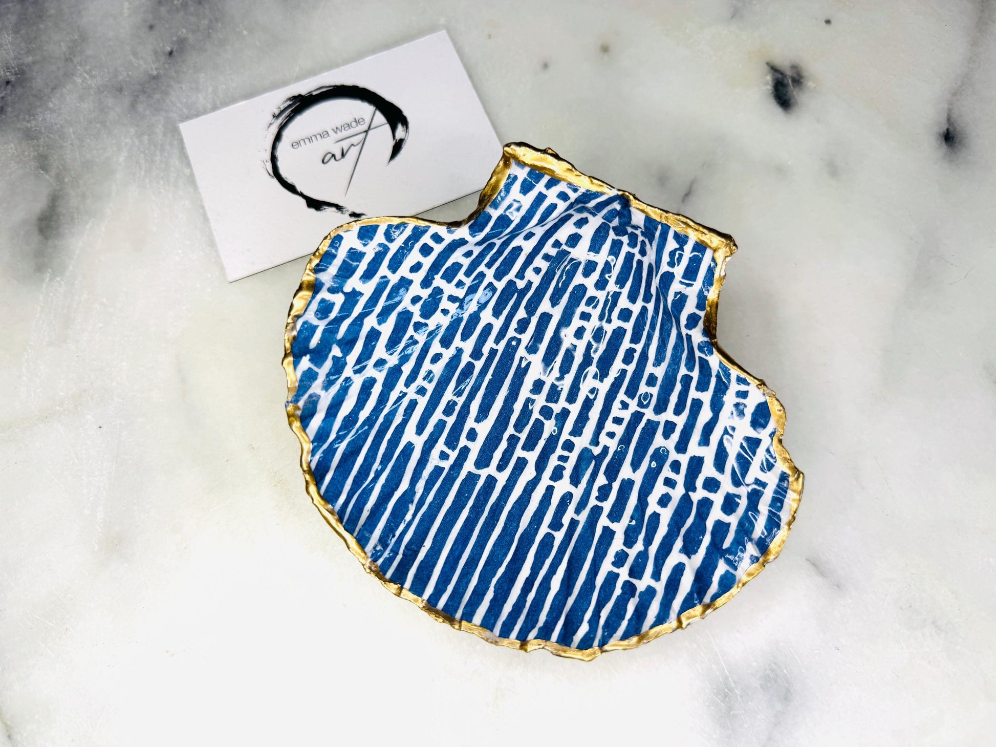 Handmade blue and white scallop shell trinket dish with gold leaf edging, crafted from a genuine Dorset shell and sealed with glossy resin. Coastal ring dish and jewellery holder featuring elegant blue line design, displayed in gift packaging. Artisan shell decor handmade in Surrey, perfect for coastal home styling, wedding gifts or nautical themed interiors.