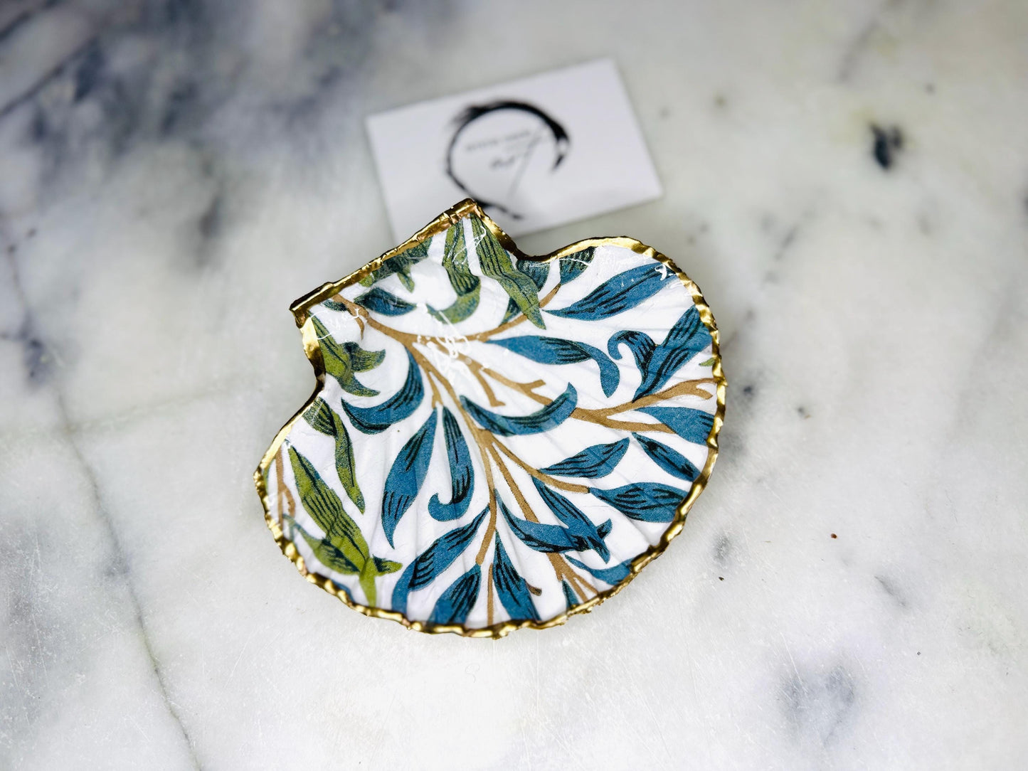 Handmade Dorset scallop shell trinket dish featuring William Morris Willow Bough design in soft blue and green tones. Decorative shell jewellery dish finished with hand-applied liquid gold leaf edging and glossy resin. Coastal inspired ring holder with botanical Arts and Crafts pattern and natural shell shape, styled as elegant bathroom décor and heritage home accessory.