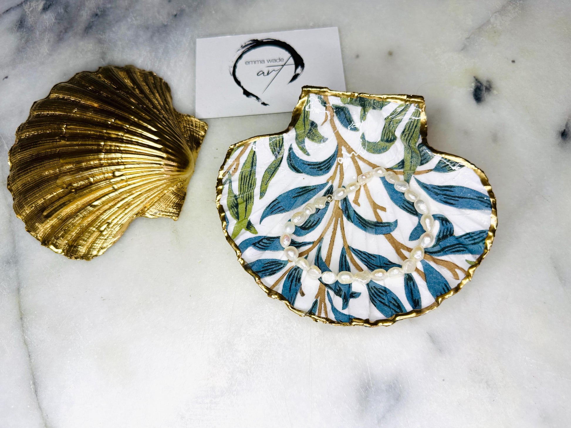 Handmade Dorset scallop shell trinket dish featuring William Morris Willow Bough design in soft blue and green tones. Decorative shell jewellery dish finished with hand-applied liquid gold leaf edging and glossy resin. Coastal inspired ring holder with botanical Arts and Crafts pattern and natural shell shape, styled as elegant bathroom décor and heritage home accessory.