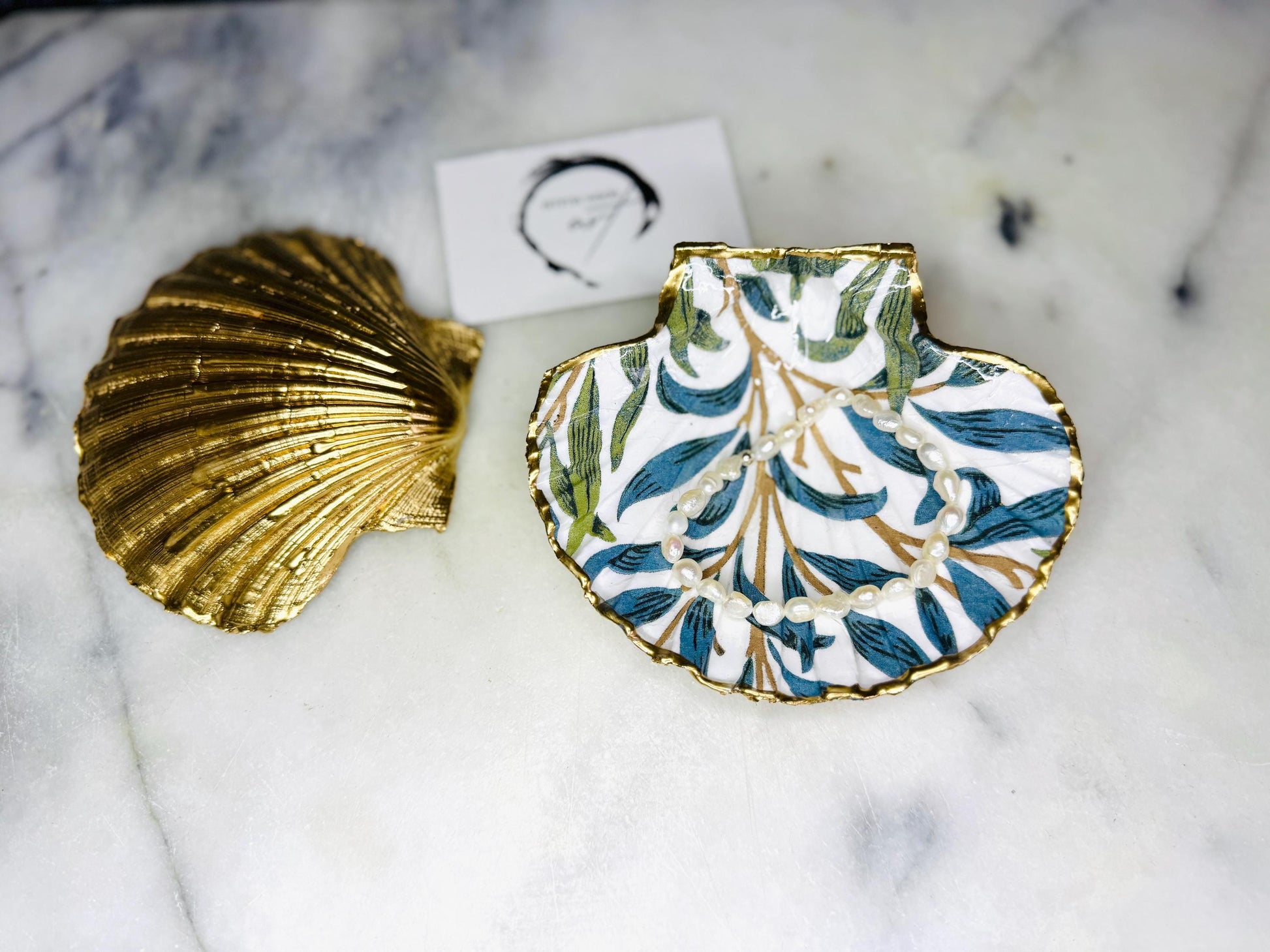 Handmade Dorset scallop shell trinket dish featuring William Morris Willow Bough design in soft blue and green tones. Decorative shell jewellery dish finished with hand-applied liquid gold leaf edging and glossy resin. Coastal inspired ring holder with botanical Arts and Crafts pattern and natural shell shape, styled as elegant bathroom décor and heritage home accessory.