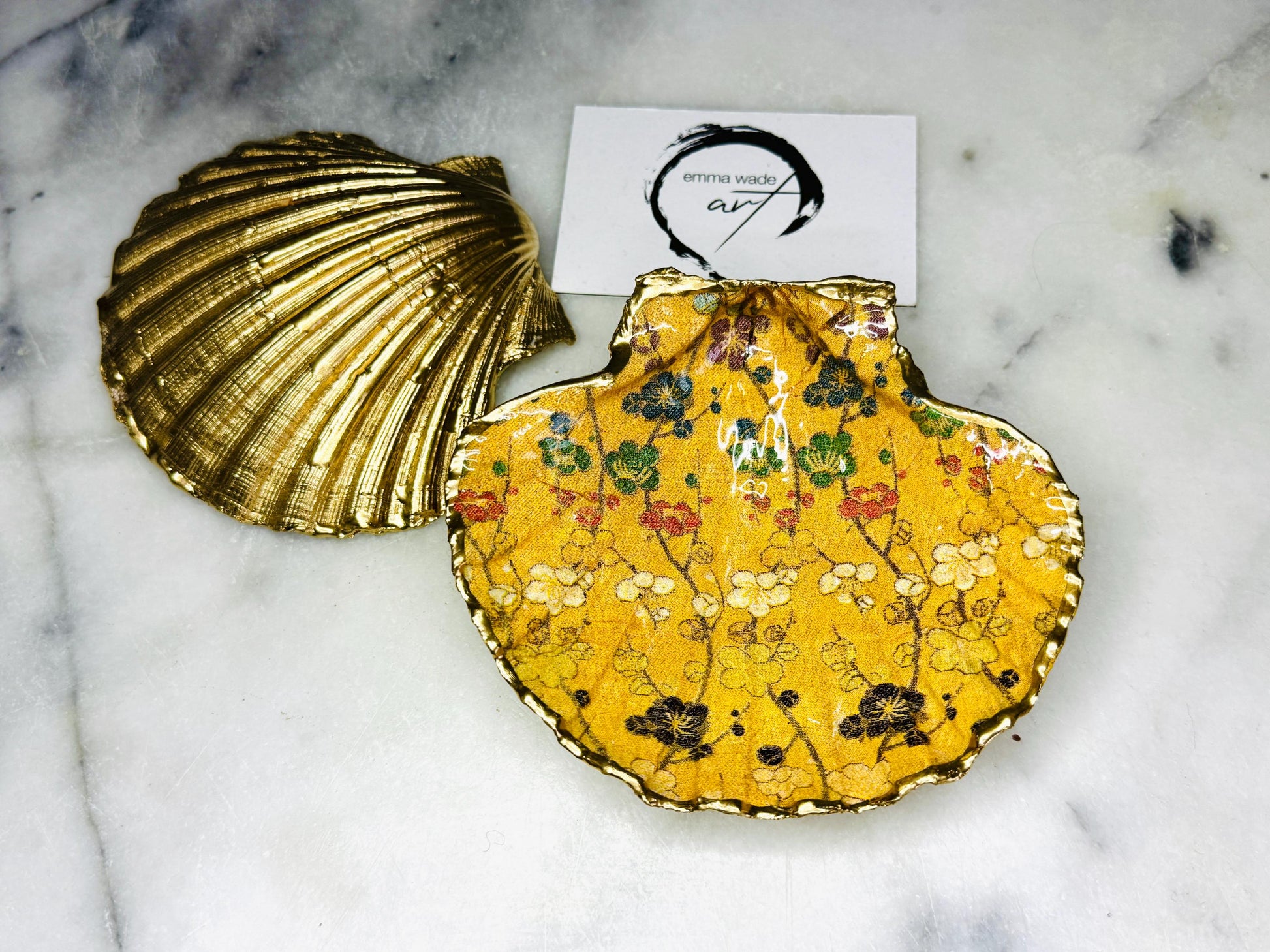 Handmade Dorset scallop shell trinket dish with Japanese plum blossom floral design on golden yellow background, finished with real liquid gold leaf edging and sealed in glossy resin. Unique coastal home decor piece, ideal as a jewellery dish, ring holder, or trinket tray. Sustainably sourced shell, artisan crafted in the UK, perfect gift for birthdays, weddings, anniversaries, or elegant dressing table styling.