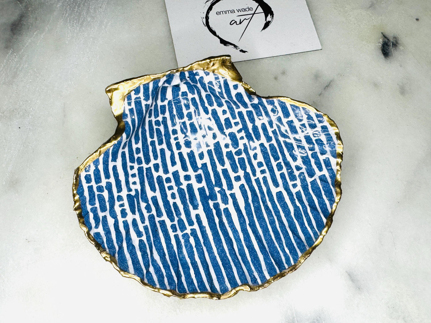 Handmade blue and white scallop shell trinket dish with gold leaf edging, crafted from a genuine Dorset shell and sealed with glossy resin. Coastal ring dish and jewellery holder featuring elegant blue line design, displayed in gift packaging. Artisan shell decor handmade in Surrey, perfect for coastal home styling, wedding gifts or nautical themed interiors.