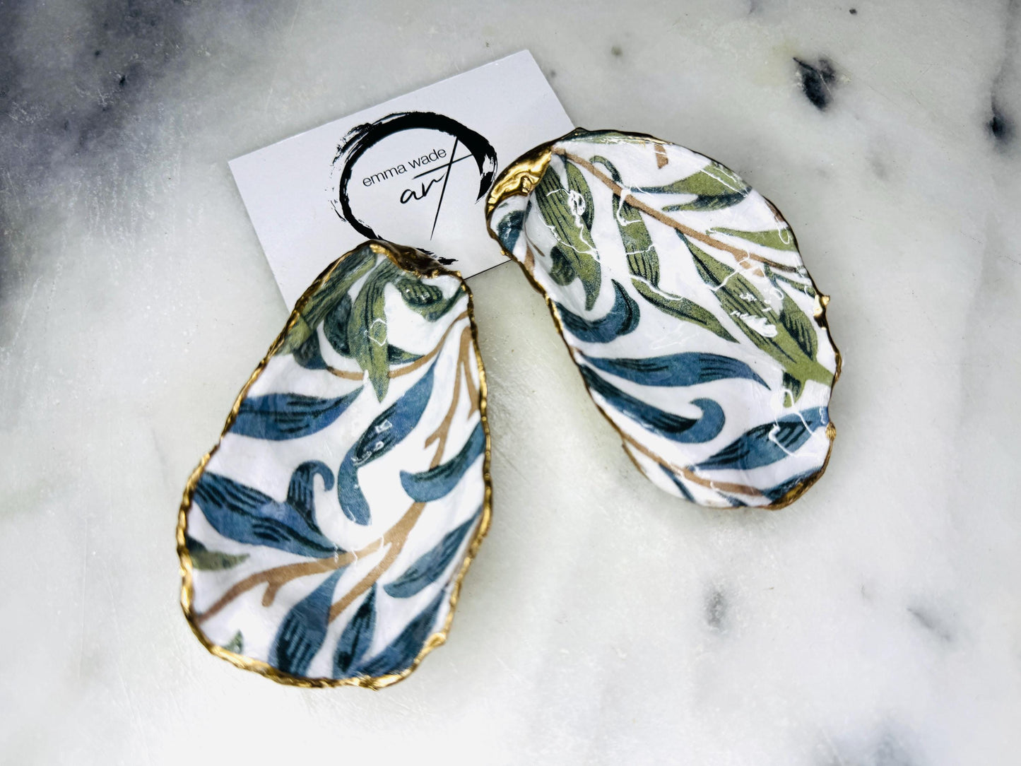 Handmade Dorset oyster shell trinket dish featuring William Morris Willow Bough botanical design in soft blue and sage green tones. Decorative jewellery holder finished with hand-applied liquid gold leaf edging and glossy resin. Coastal heritage décor shell dish styled as a ring holder and elegant bathroom accessory with natural oyster shell shape.