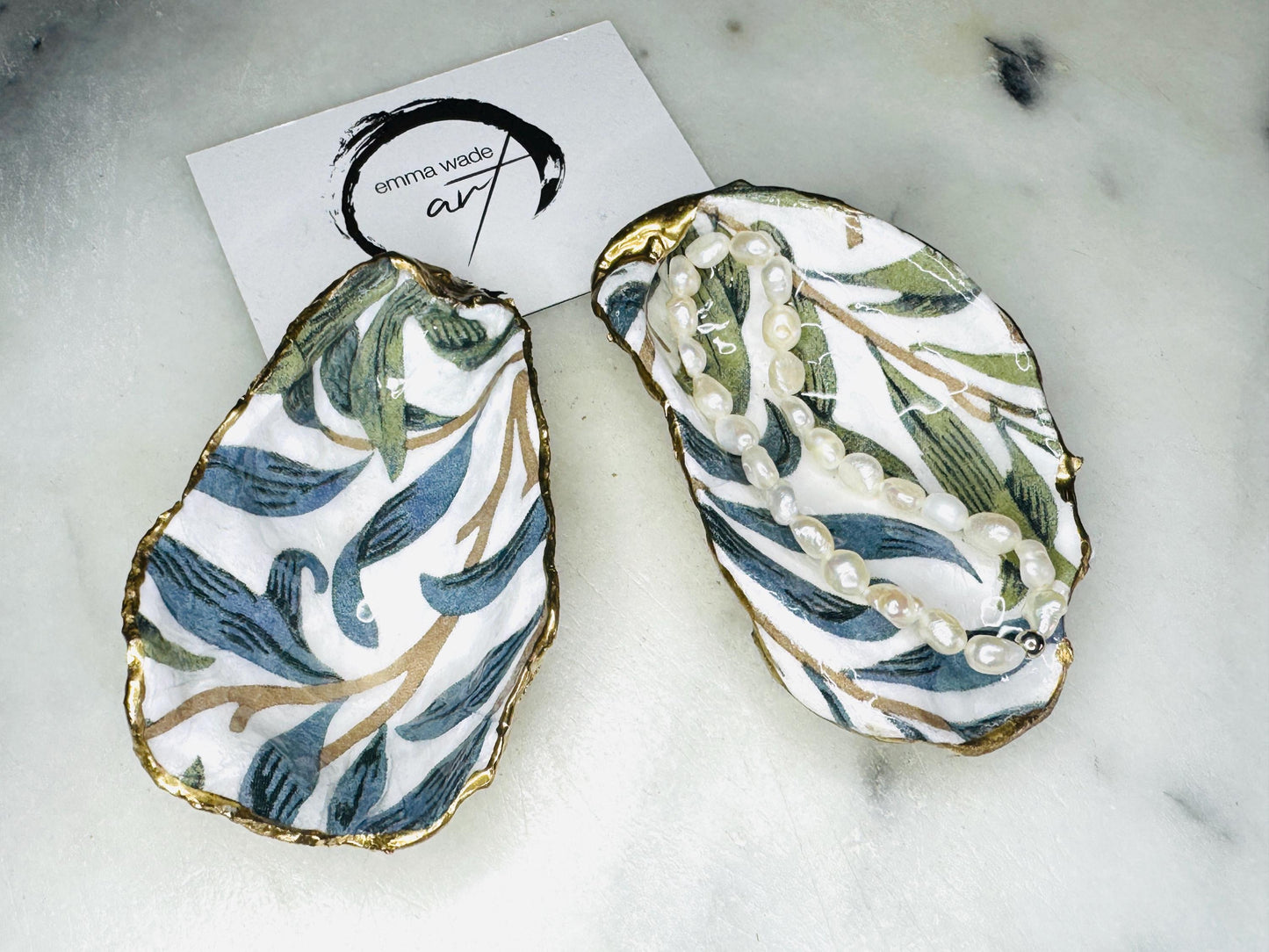 Handmade Dorset oyster shell trinket dish featuring William Morris Willow Bough botanical design in soft blue and sage green tones. Decorative jewellery holder finished with hand-applied liquid gold leaf edging and glossy resin. Coastal heritage décor shell dish styled as a ring holder and elegant bathroom accessory with natural oyster shell shape.