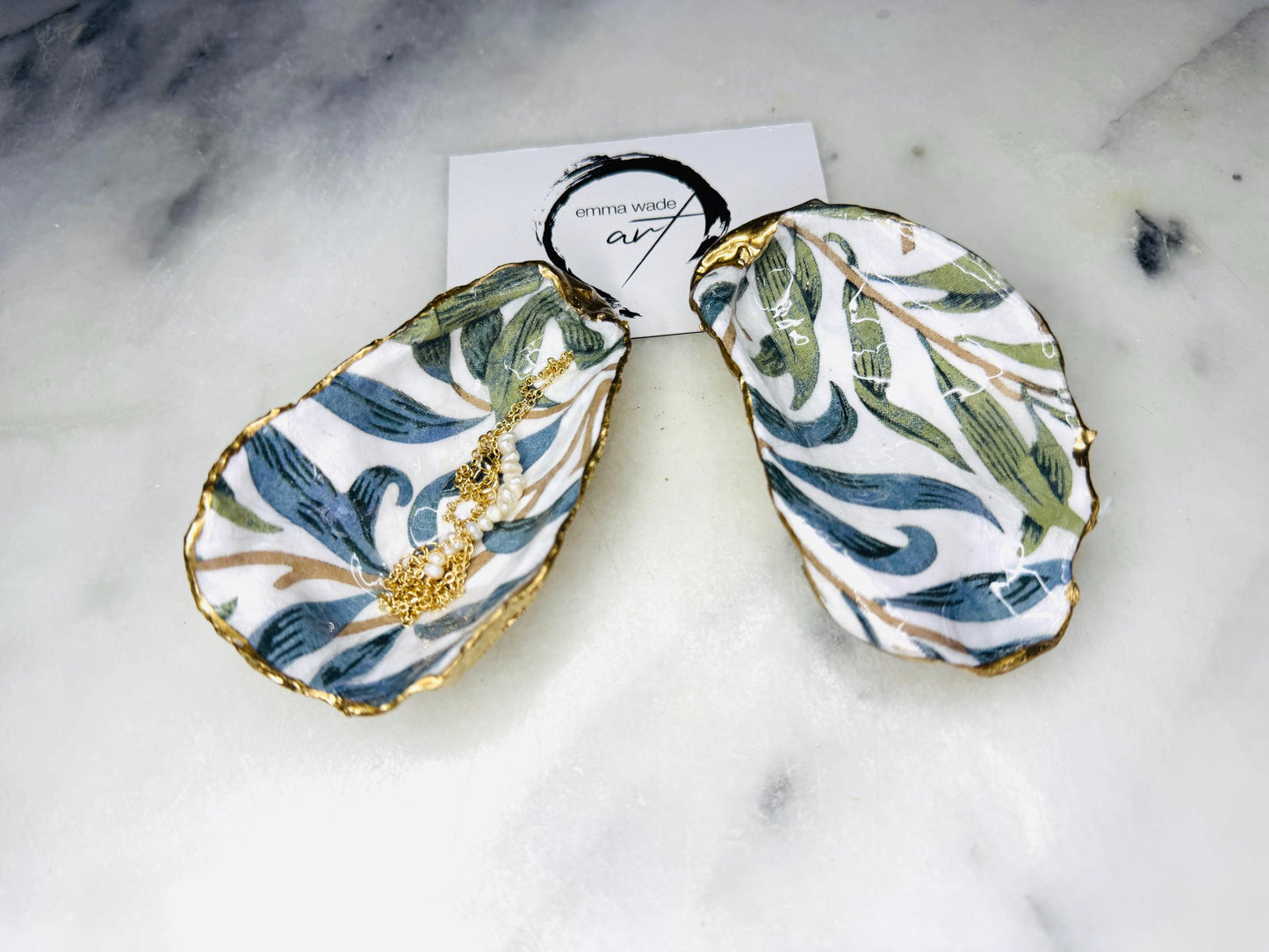 Handmade Dorset oyster shell trinket dish featuring William Morris Willow Bough botanical design in soft blue and sage green tones. Decorative jewellery holder finished with hand-applied liquid gold leaf edging and glossy resin. Coastal heritage décor shell dish styled as a ring holder and elegant bathroom accessory with natural oyster shell shape.