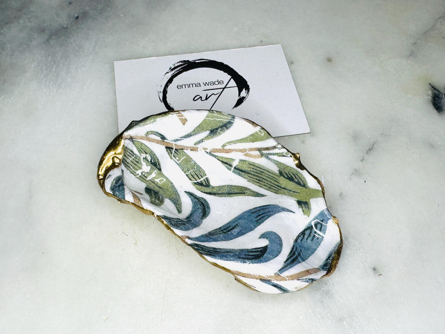 Handmade Dorset oyster shell trinket dish featuring William Morris Willow Bough botanical design in soft blue and sage green tones. Decorative jewellery holder finished with hand-applied liquid gold leaf edging and glossy resin. Coastal heritage décor shell dish styled as a ring holder and elegant bathroom accessory with natural oyster shell shape.