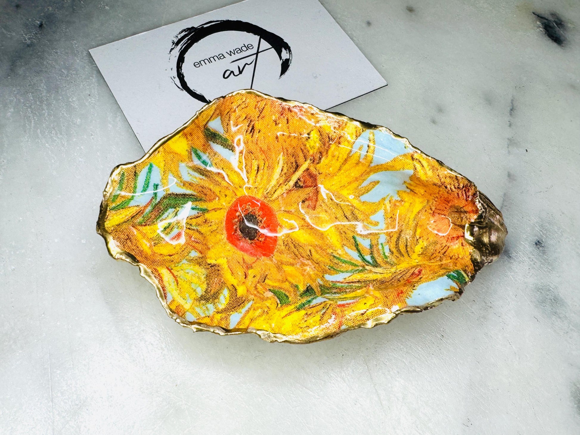 Hand-painted Vincent Van Gogh Sunflowers oyster shell trinket dish with hand-applied liquid gold leaf edging and high gloss resin finish. Natural Dorset oyster shell jewellery holder featuring vibrant yellow sunflower design, styled on marble surface as a ring dish, coastal decor accent and luxury handmade gift.