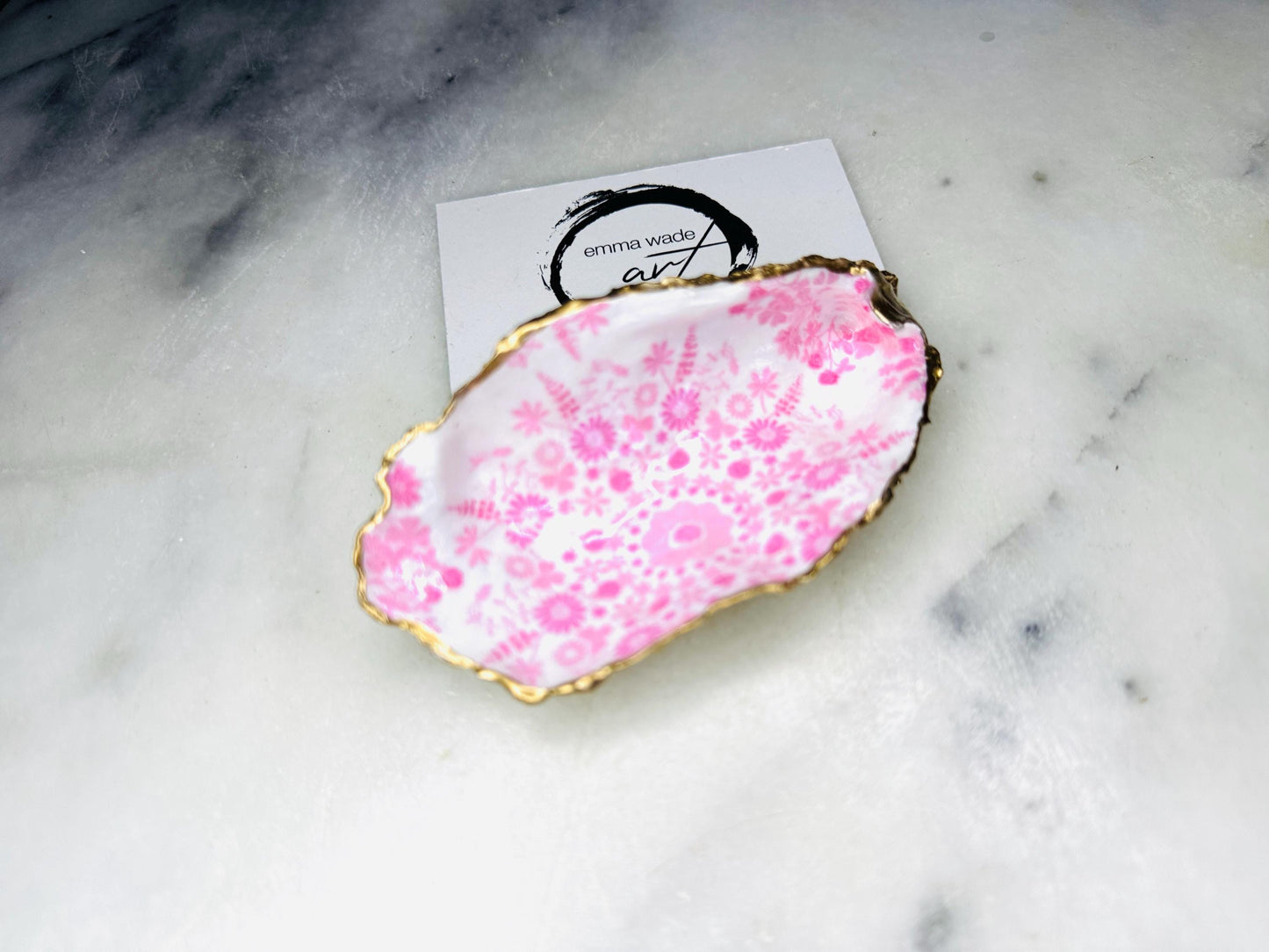 Floral oyster shell ring holder with pink lily design and gold leaf edge. Handmade shell jewellery dish, ideal as a trinket tray or shell ring tray. Each shell is unique, approx. 9–11cm. Perfect for displaying rings, earrings, or cufflinks, or as a decorative piece in the bathroom or bedroom. A versatile gift for weddings, anniversaries, bridesmaids, or new homes. Can also be used as a tealight holder, spoon rest, or small salt and pepper dish.
