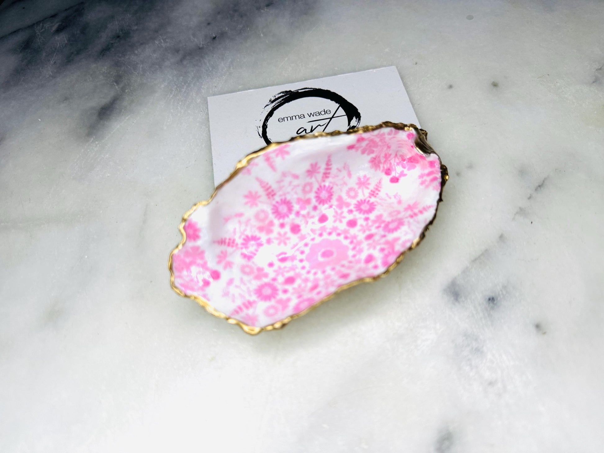 Floral oyster shell ring holder with pink lily design and gold leaf edge. Handmade shell jewellery dish, ideal as a trinket tray or shell ring tray. Each shell is unique, approx. 9–11cm. Perfect for displaying rings, earrings, or cufflinks, or as a decorative piece in the bathroom or bedroom. A versatile gift for weddings, anniversaries, bridesmaids, or new homes. Can also be used as a tealight holder, spoon rest, or small salt and pepper dish.