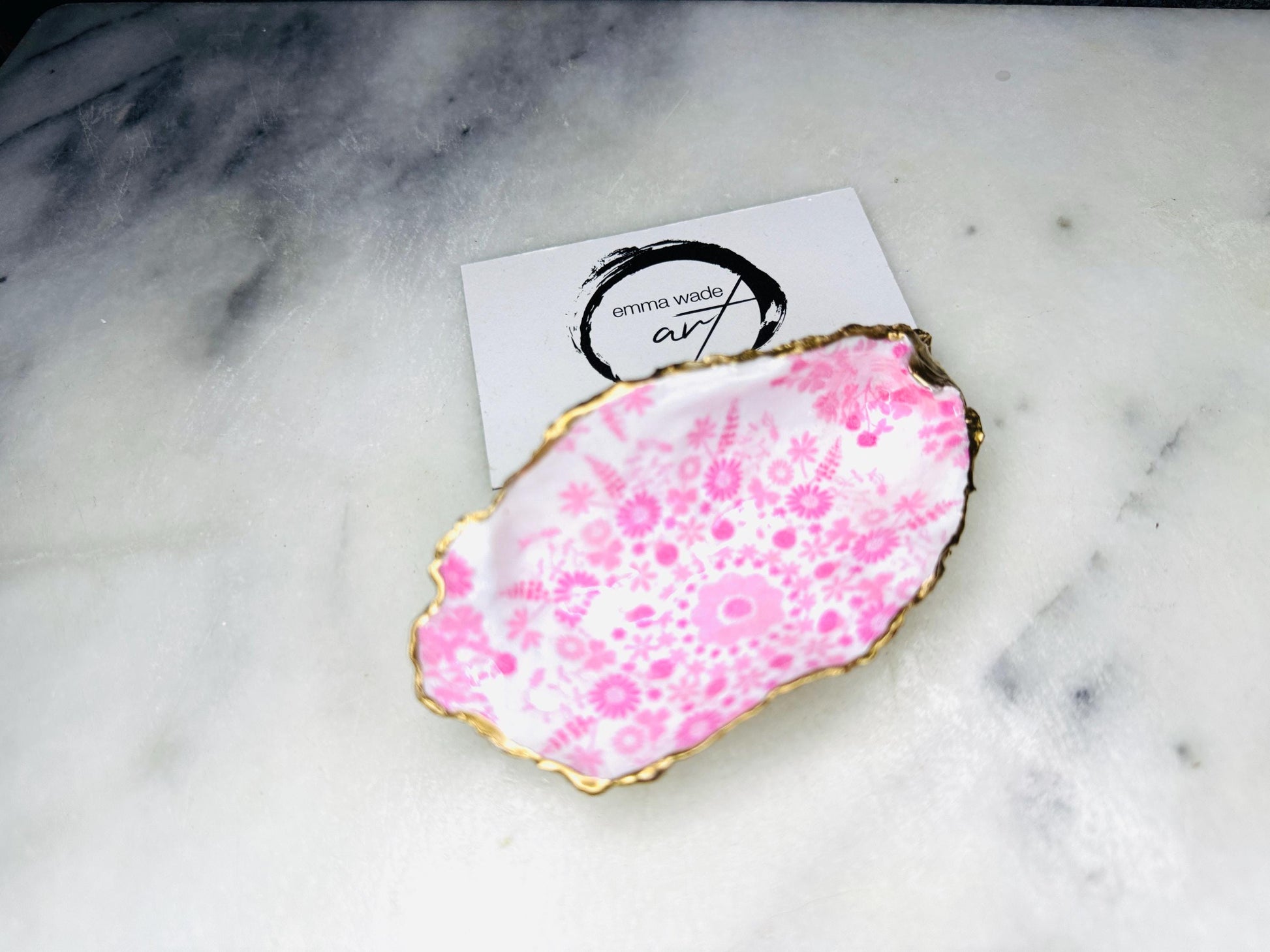 Floral oyster shell ring holder with pink lily design and gold leaf edge. Handmade shell jewellery dish, ideal as a trinket tray or shell ring tray. Each shell is unique, approx. 9–11cm. Perfect for displaying rings, earrings, or cufflinks, or as a decorative piece in the bathroom or bedroom. A versatile gift for weddings, anniversaries, bridesmaids, or new homes. Can also be used as a tealight holder, spoon rest, or small salt and pepper dish.