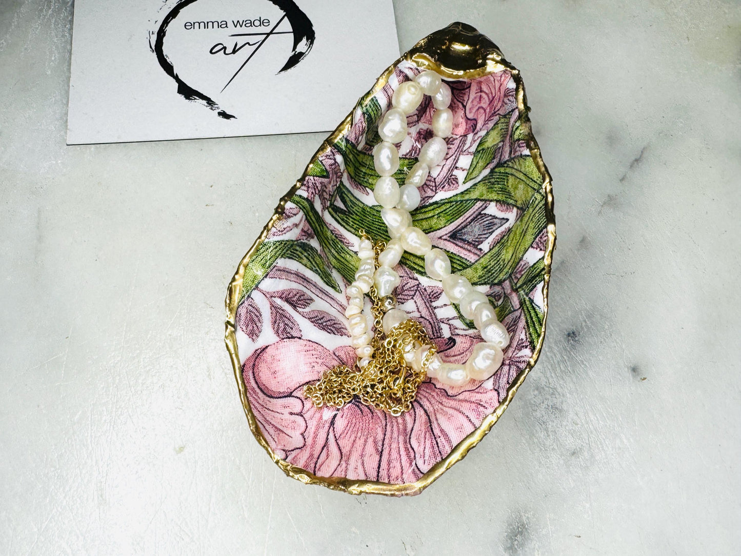Single handcrafted Dorset oyster shell trinket dish featuring the William Morris Pink Pimpernel design in pink and green tones, edged with liquid gold leaf and sealed in glossy resin. Sold individually, this natural oyster shell jewellery holder is ideal for rings or earrings and makes a unique coastal gift or wedding favour.