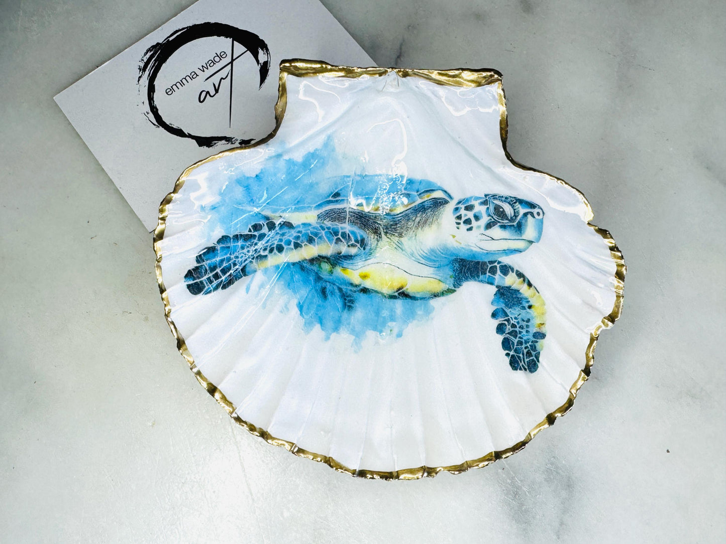 Handmade scallop shell trinket dish featuring a blue sea turtle illustration, finished with high gloss crystal resin and optional gilded gold leaf edges. Coastal home decor shell dish for jewellery, rings, trinkets or bedside storage. Nautical ocean inspired decorative shell, handmade in the UK using sustainably sourced shells from the Dorset coastline. Ideal coastal gift for ocean lovers and beach house interiors.