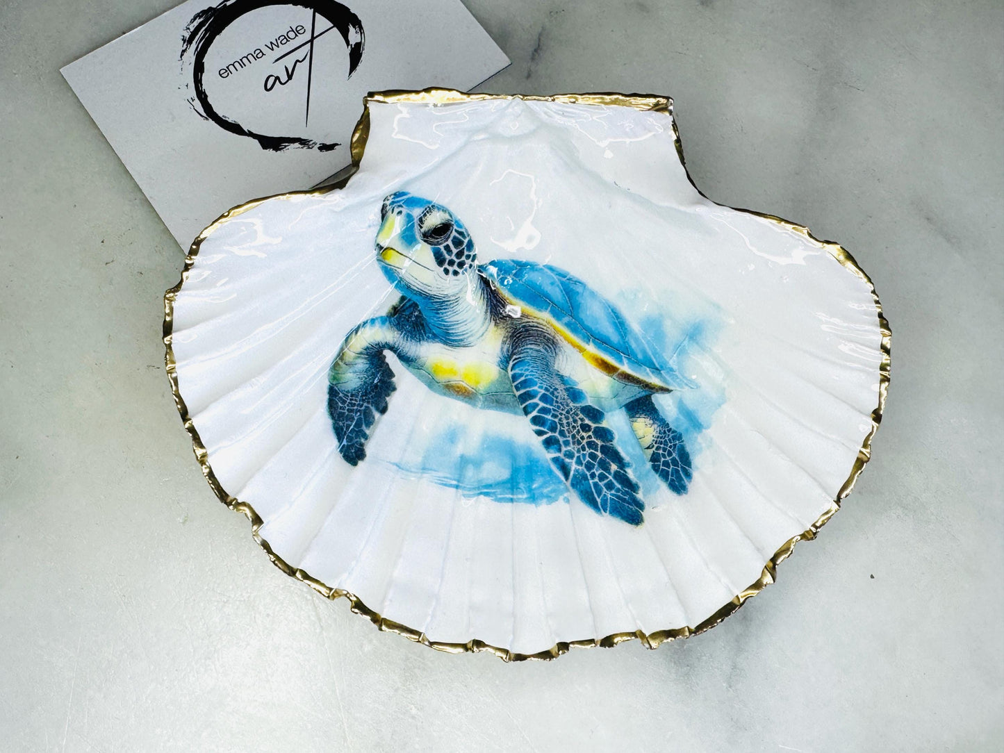 Handmade scallop shell trinket dish featuring a blue sea turtle illustration, finished with high gloss crystal resin and optional gilded gold leaf edges. Coastal home decor shell dish for jewellery, rings, trinkets or bedside storage. Nautical ocean inspired decorative shell, handmade in the UK using sustainably sourced shells from the Dorset coastline. Ideal coastal gift for ocean lovers and beach house interiors.