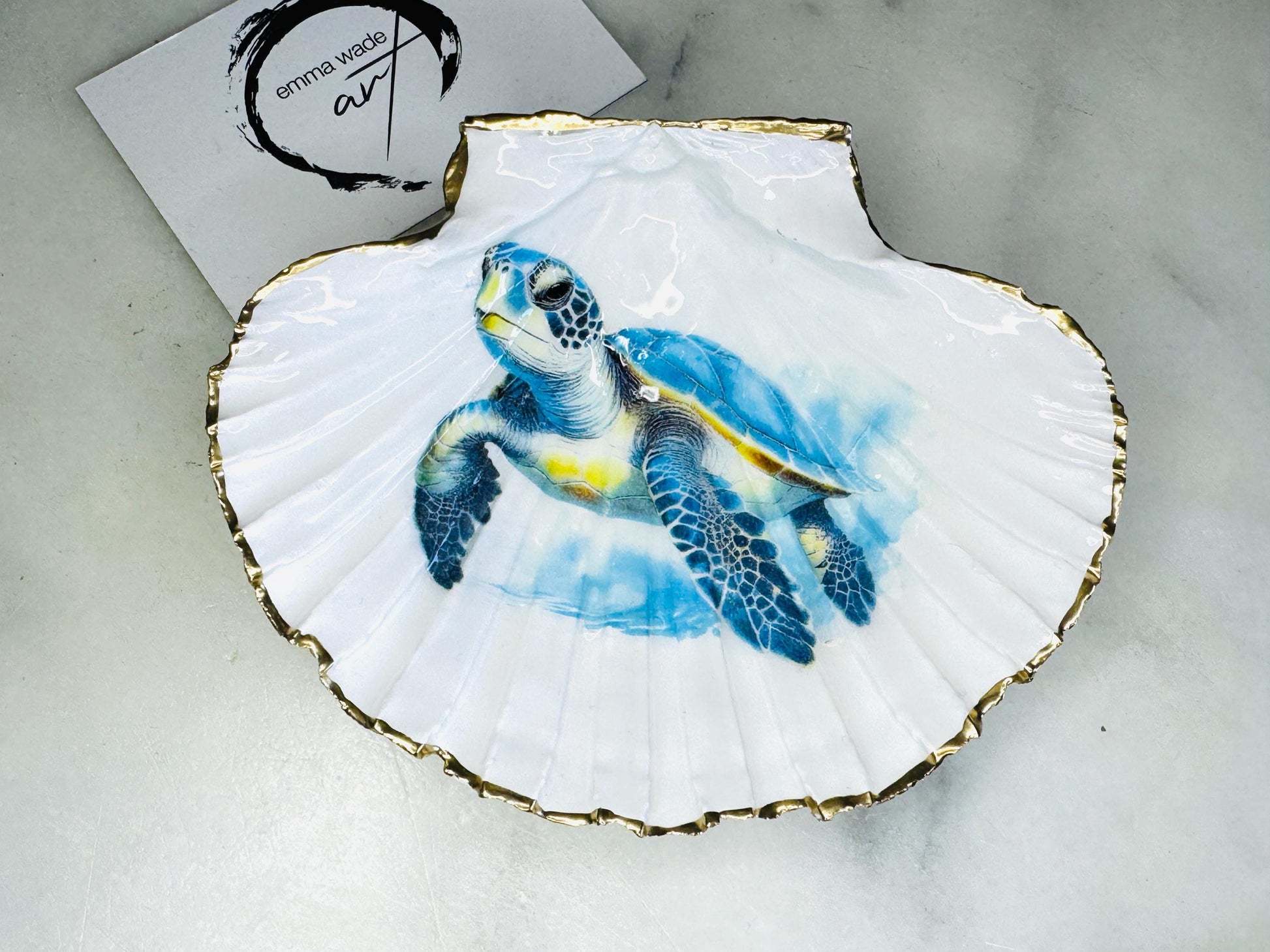Handmade scallop shell trinket dish featuring a blue sea turtle illustration, finished with high gloss crystal resin and optional gilded gold leaf edges. Coastal home decor shell dish for jewellery, rings, trinkets or bedside storage. Nautical ocean inspired decorative shell, handmade in the UK using sustainably sourced shells from the Dorset coastline. Ideal coastal gift for ocean lovers and beach house interiors.