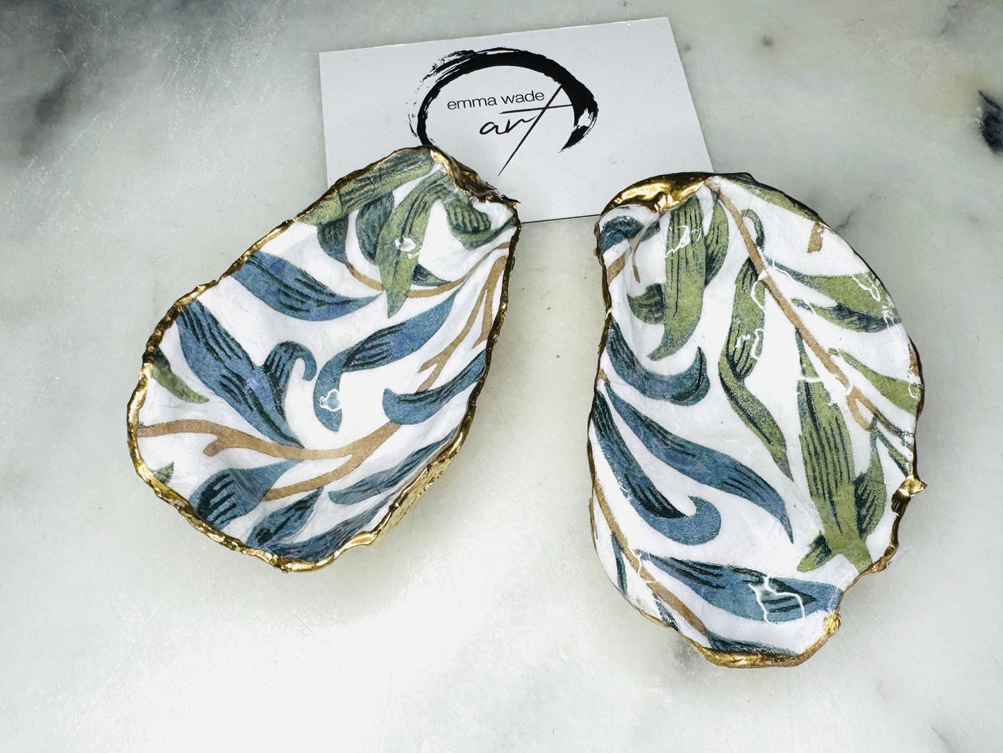 Handmade Dorset oyster shell trinket dish featuring William Morris Willow Bough botanical design in soft blue and sage green tones. Decorative jewellery holder finished with hand-applied liquid gold leaf edging and glossy resin. Coastal heritage décor shell dish styled as a ring holder and elegant bathroom accessory with natural oyster shell shape.