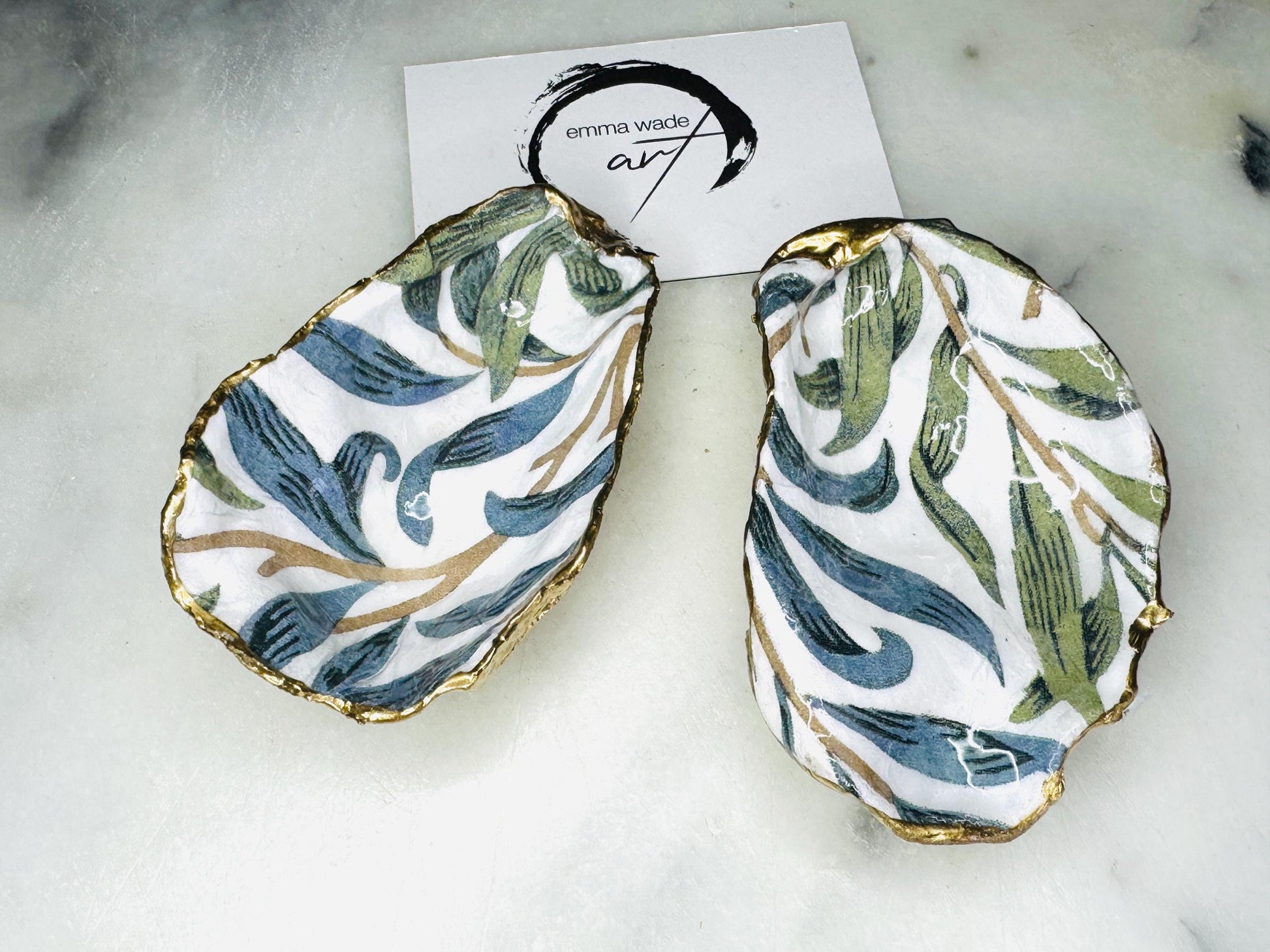 Handmade Dorset oyster shell trinket dish featuring William Morris Willow Bough botanical design in soft blue and sage green tones. Decorative jewellery holder finished with hand-applied liquid gold leaf edging and glossy resin. Coastal heritage décor shell dish styled as a ring holder and elegant bathroom accessory with natural oyster shell shape.