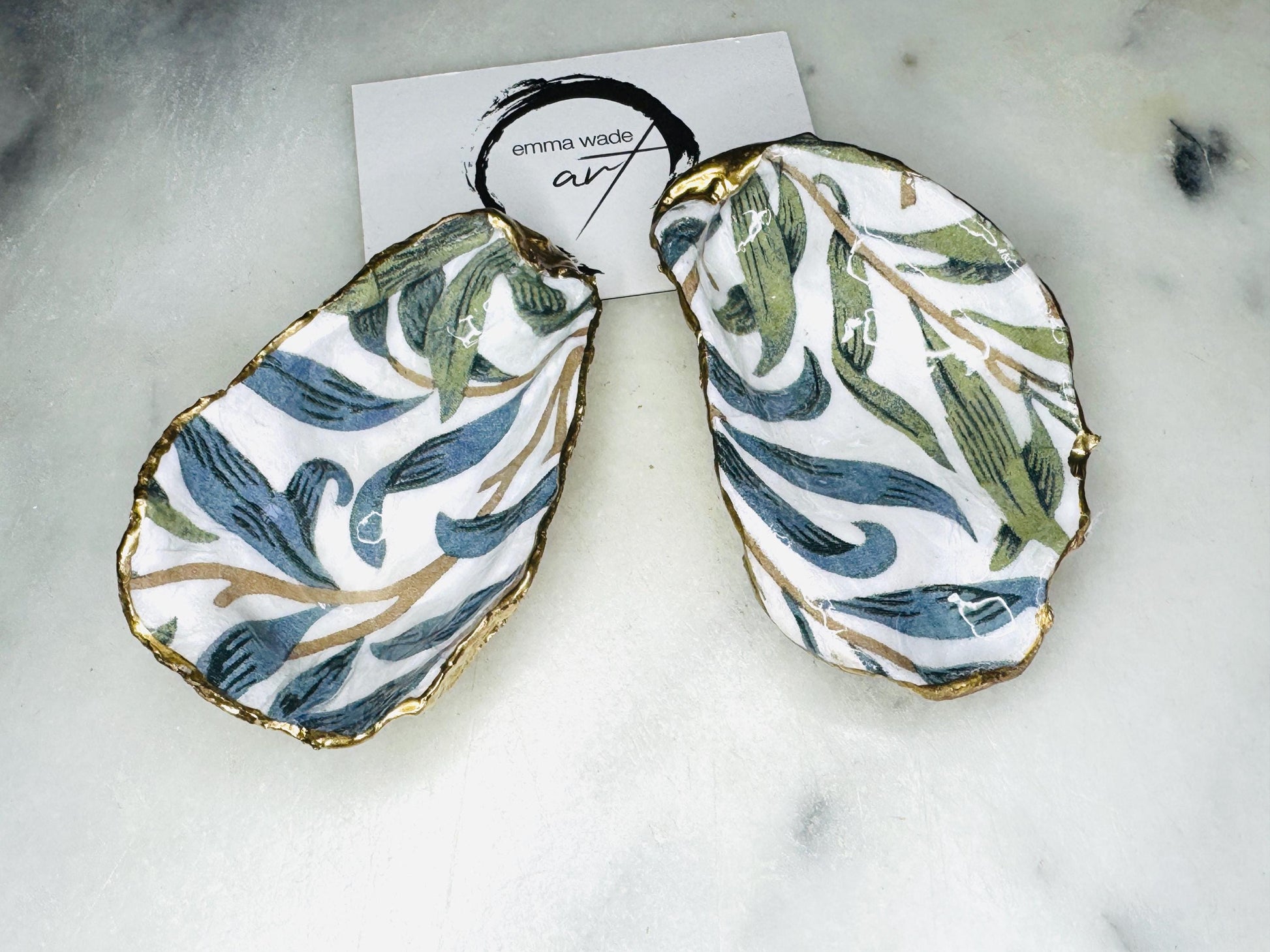 Handmade Dorset oyster shell trinket dish featuring William Morris Willow Bough botanical design in soft blue and sage green tones. Decorative jewellery holder finished with hand-applied liquid gold leaf edging and glossy resin. Coastal heritage décor shell dish styled as a ring holder and elegant bathroom accessory with natural oyster shell shape.