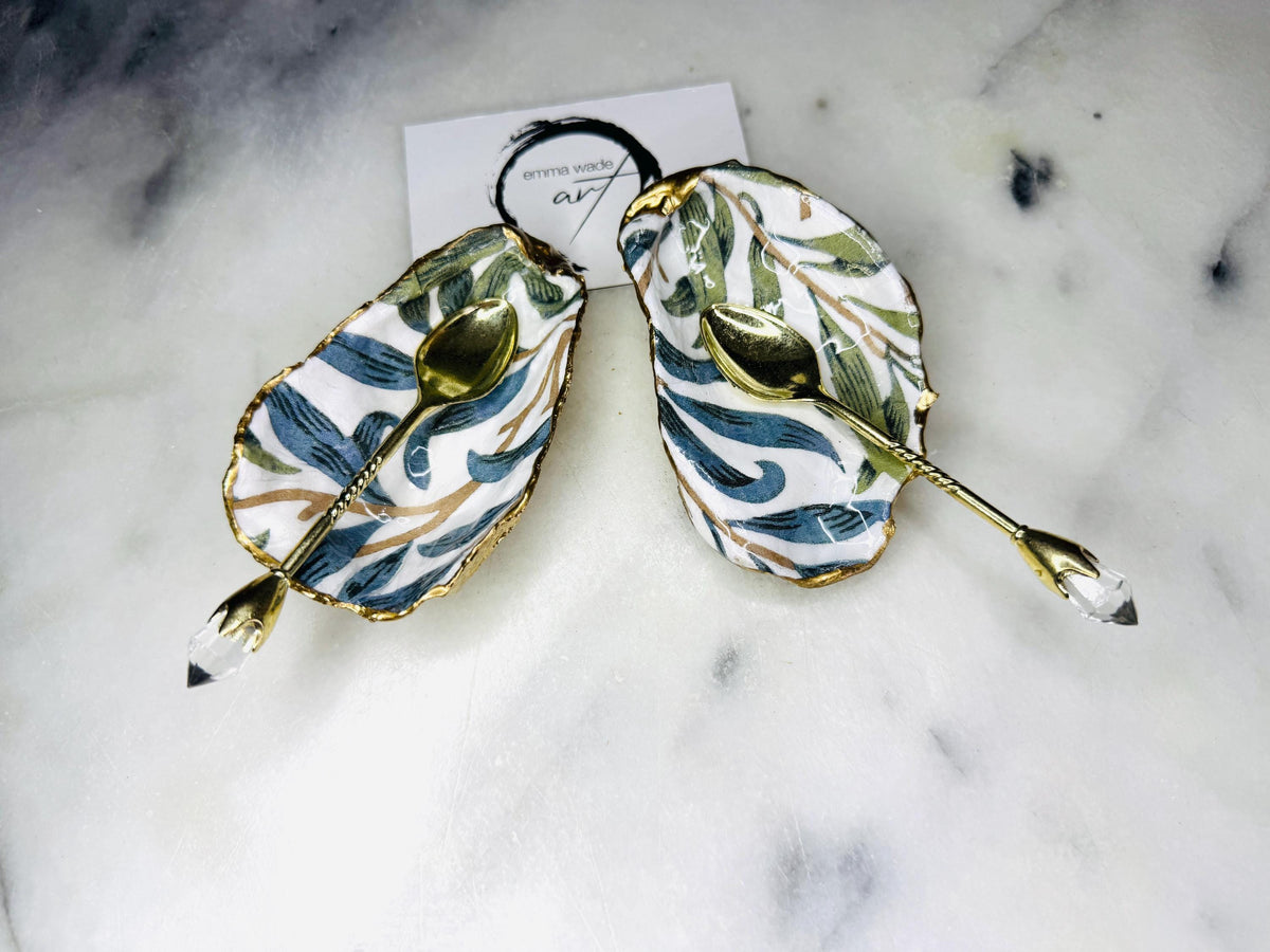William Morris Willow Bough oyster shell salt and pepper pinch pots, sold as a pair. Natural Dorset cupped oyster shells featuring green and blue heritage pattern, hand-finished with gold leaf edging and sealed with glossy resin. Styled with optional ornate gold crystal spoons on a marble surface as elegant coastal table decor and luxury host gift. Mother’s Day gift