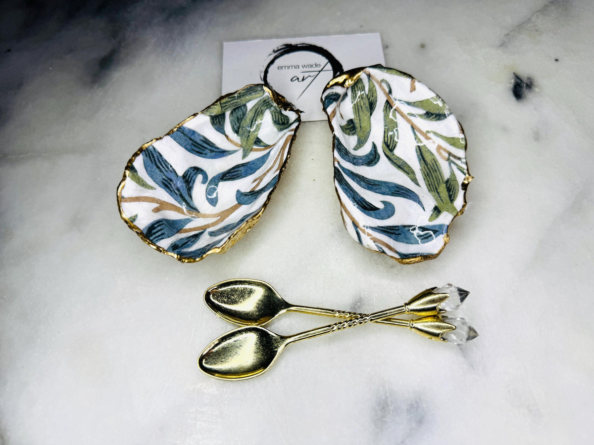 William Morris Willow Bough oyster shell salt and pepper pinch pots, sold as a pair. Natural Dorset cupped oyster shells featuring green and blue heritage pattern, hand-finished with gold leaf edging and sealed with glossy resin. Styled with optional ornate gold crystal spoons on a marble surface as elegant coastal table decor and luxury host gift. Mother’s Day gift
