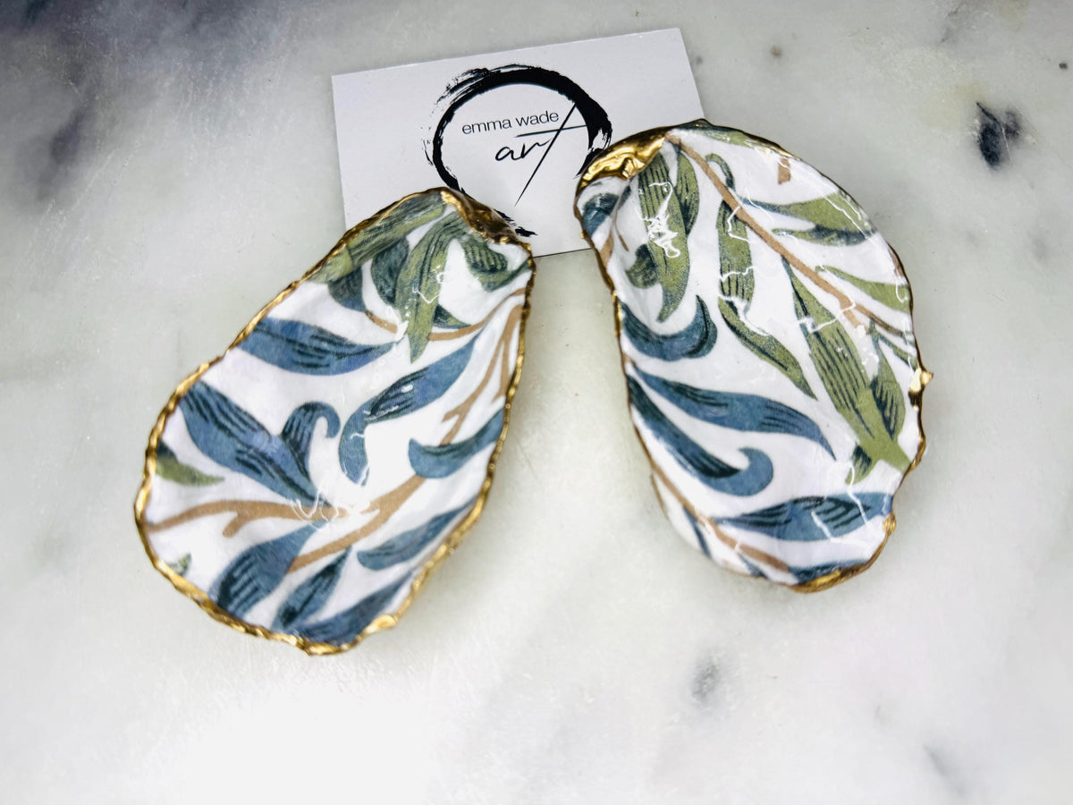 William Morris Willow Bough oyster shell salt and pepper pinch pots, sold as a pair. Natural Dorset cupped oyster shells featuring green and blue heritage pattern, hand-finished with gold leaf edging and sealed with glossy resin. Styled with optional ornate gold crystal spoons on a marble surface as elegant coastal table decor and luxury host gift. Mother’s Day gift