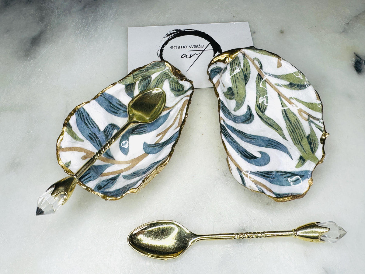 William Morris Willow Bough oyster shell salt and pepper pinch pots, sold as a pair. Natural Dorset cupped oyster shells featuring green and blue heritage pattern, hand-finished with gold leaf edging and sealed with glossy resin. Styled with optional ornate gold crystal spoons on a marble surface as elegant coastal table decor and luxury host gift. Mother’s Day gift