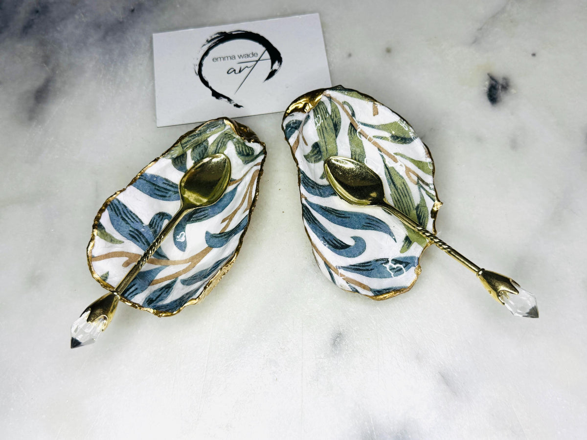 William Morris Willow Bough oyster shell salt and pepper pinch pots, sold as a pair. Natural Dorset cupped oyster shells featuring green and blue heritage pattern, hand-finished with gold leaf edging and sealed with glossy resin. Styled with optional ornate gold crystal spoons on a marble surface as elegant coastal table decor and luxury host gift. Mother’s Day gift