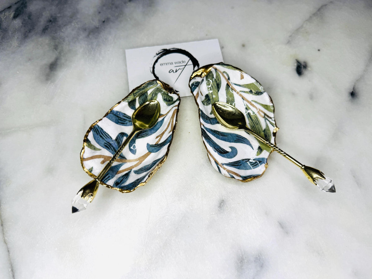 William Morris Willow Bough oyster shell salt and pepper pinch pots, sold as a pair. Natural Dorset cupped oyster shells featuring green and blue heritage pattern, hand-finished with gold leaf edging and sealed with glossy resin. Styled with optional ornate gold crystal spoons on a marble surface as elegant coastal table decor and luxury host gift. Mother’s Day gift