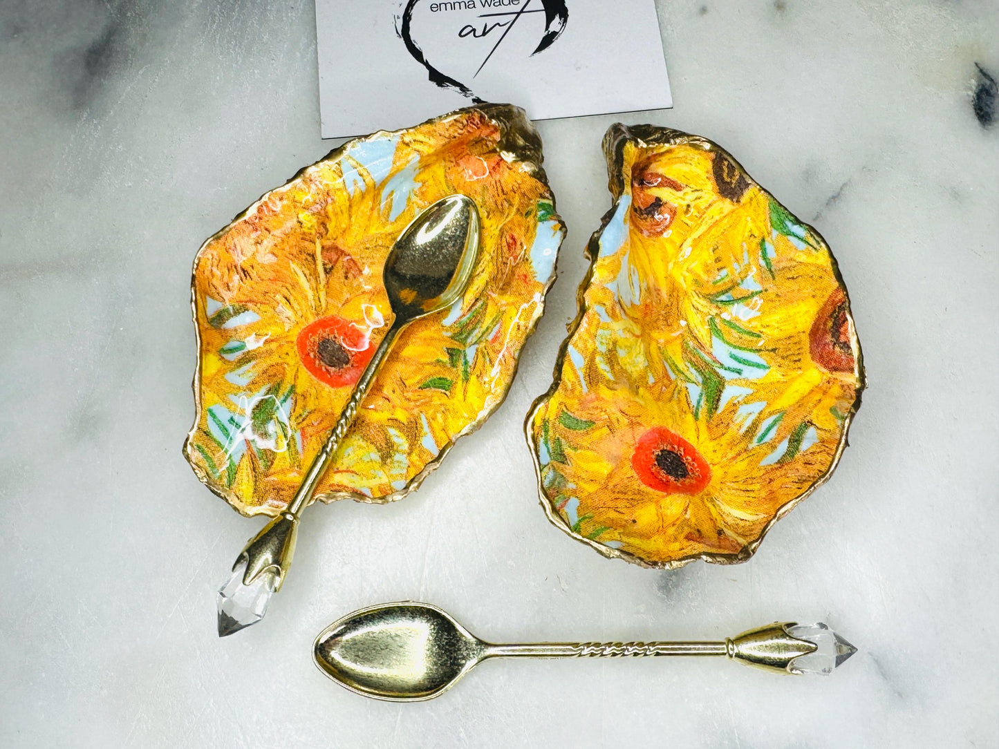 Pair of oyster shell salt and pepper dishes inspired by Vincent Van Gogh Sunflowers. Handmade from natural Dorset shells, each dish is decorated with a sunflower design, trimmed with gold leaf, and sealed for a glossy finish. Approx. 9–10cm with natural variations in shape and depth. Can be used as salt pinch pots, trinket trays, or decorative shell dishes. Optional gold crystal spoons add a luxury touch. A unique handmade gift for weddings, anniversaries, birthdays, or Christmas.