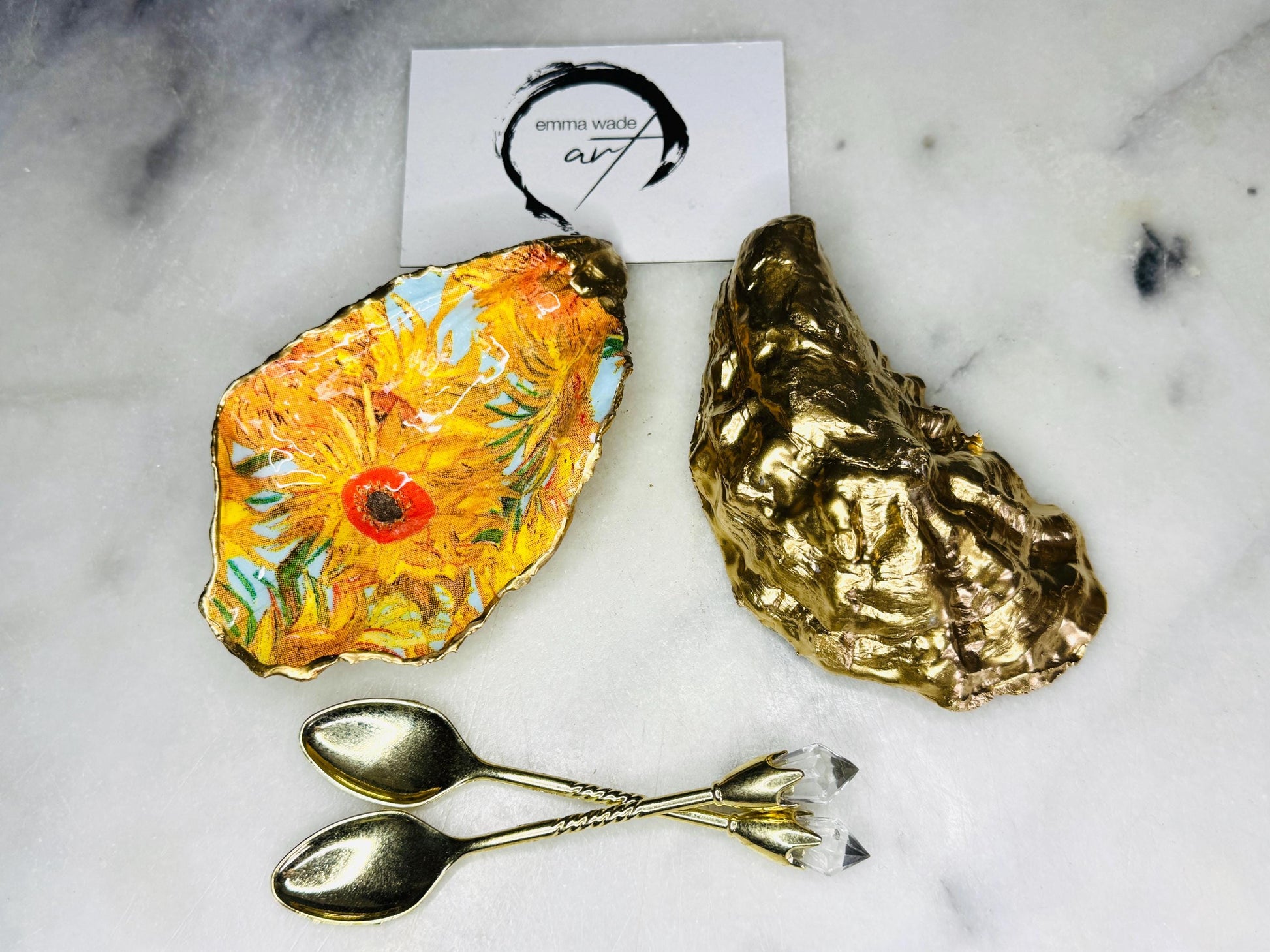 Pair of oyster shell salt and pepper dishes inspired by Vincent Van Gogh Sunflowers. Handmade from natural Dorset shells, each dish is decorated with a sunflower design, trimmed with gold leaf, and sealed for a glossy finish. Approx. 9–10cm with natural variations in shape and depth. Can be used as salt pinch pots, trinket trays, or decorative shell dishes. Optional gold crystal spoons add a luxury touch. A unique handmade gift for weddings, anniversaries, birthdays, or Christmas.