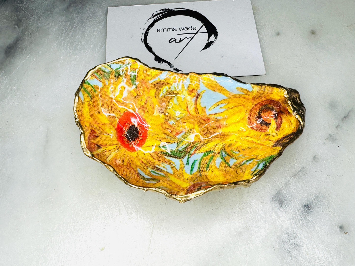 Hand-painted Vincent Van Gogh Sunflowers oyster shell trinket dish with hand-applied liquid gold leaf edging and high gloss resin finish. Natural Dorset oyster shell jewellery holder featuring vibrant yellow sunflower design, styled on marble surface as a ring dish, coastal decor accent and luxury handmade gift.