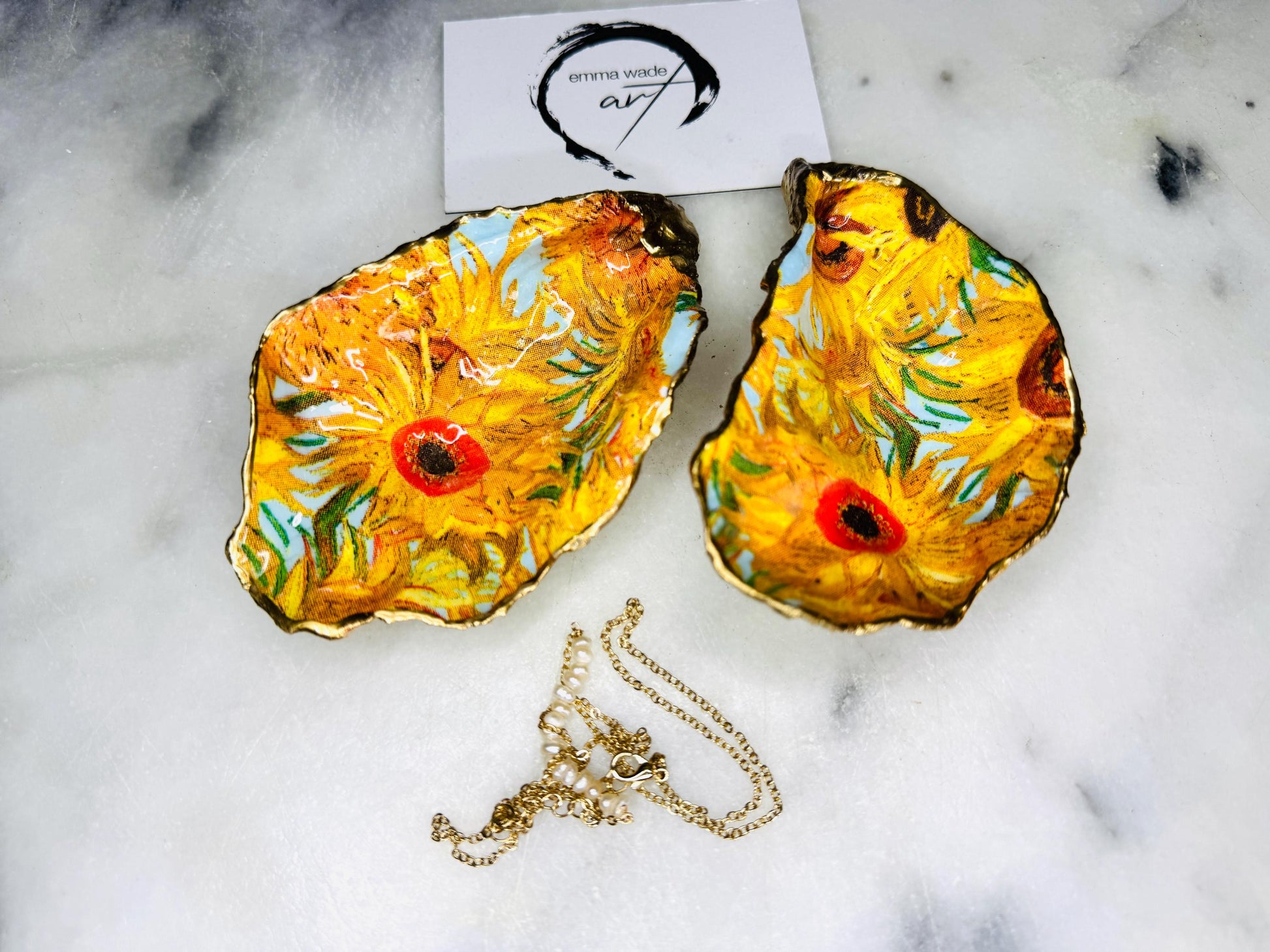Hand-painted Vincent Van Gogh Sunflowers oyster shell trinket dish with hand-applied liquid gold leaf edging and high gloss resin finish. Natural Dorset oyster shell jewellery holder featuring vibrant yellow sunflower design, styled on marble surface as a ring dish, coastal decor accent and luxury handmade gift.