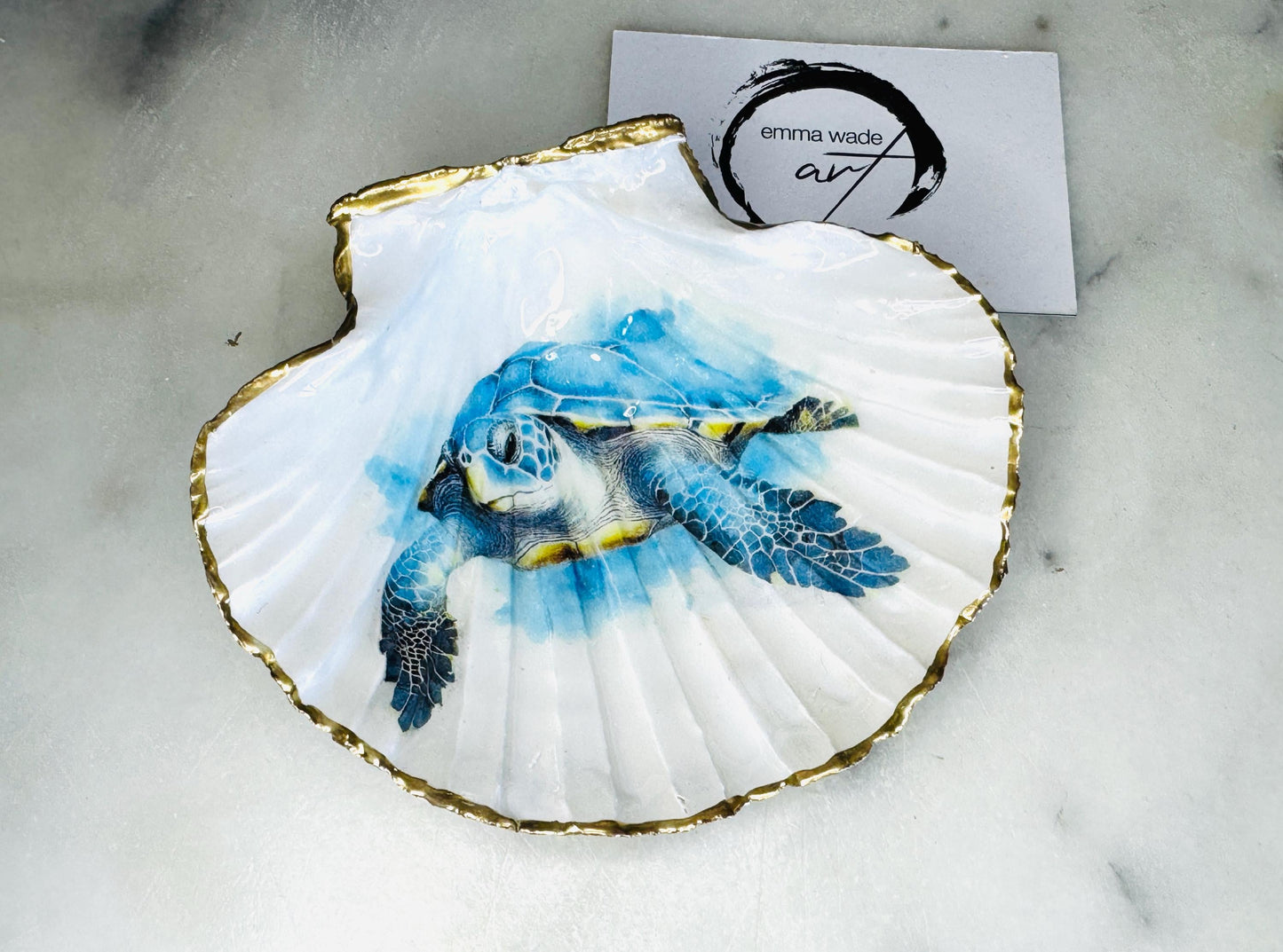 Handmade scallop shell trinket dish featuring a blue sea turtle illustration, finished with high gloss crystal resin and optional gilded gold leaf edges. Coastal home decor shell dish for jewellery, rings, trinkets or bedside storage. Nautical ocean inspired decorative shell, handmade in the UK using sustainably sourced shells from the Dorset coastline. Ideal coastal gift for ocean lovers and beach house interiors.