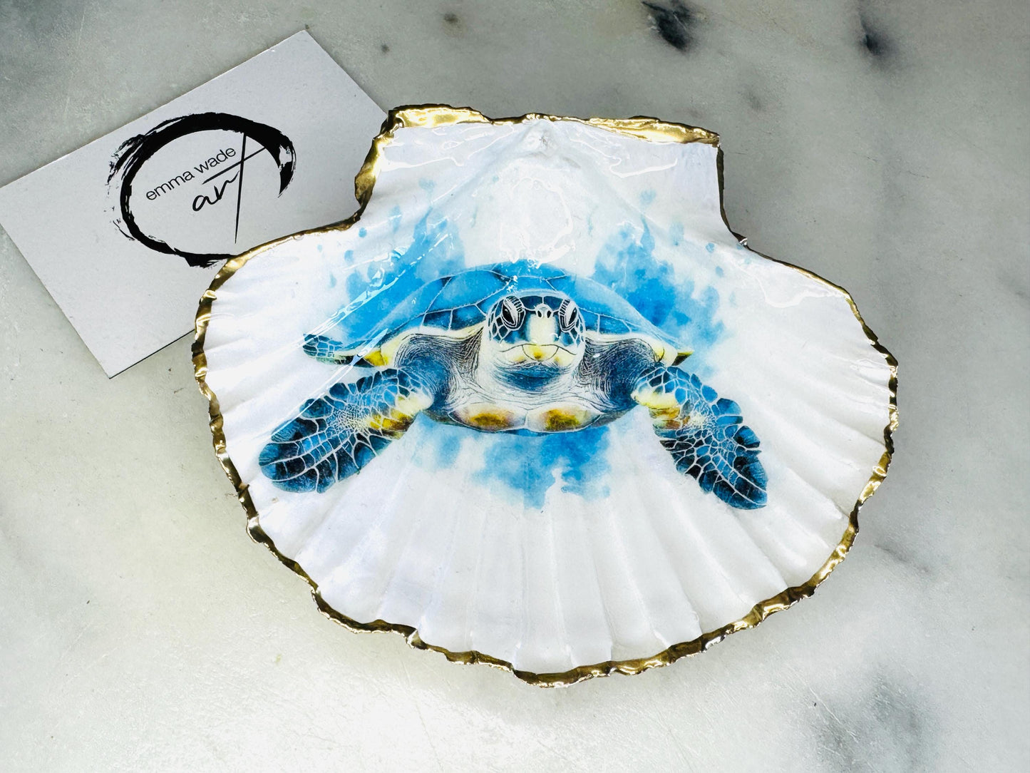 Handmade scallop shell trinket dish featuring a blue sea turtle illustration, finished with high gloss crystal resin and optional gilded gold leaf edges. Coastal home decor shell dish for jewellery, rings, trinkets or bedside storage. Nautical ocean inspired decorative shell, handmade in the UK using sustainably sourced shells from the Dorset coastline. Ideal coastal gift for ocean lovers and beach house interiors.