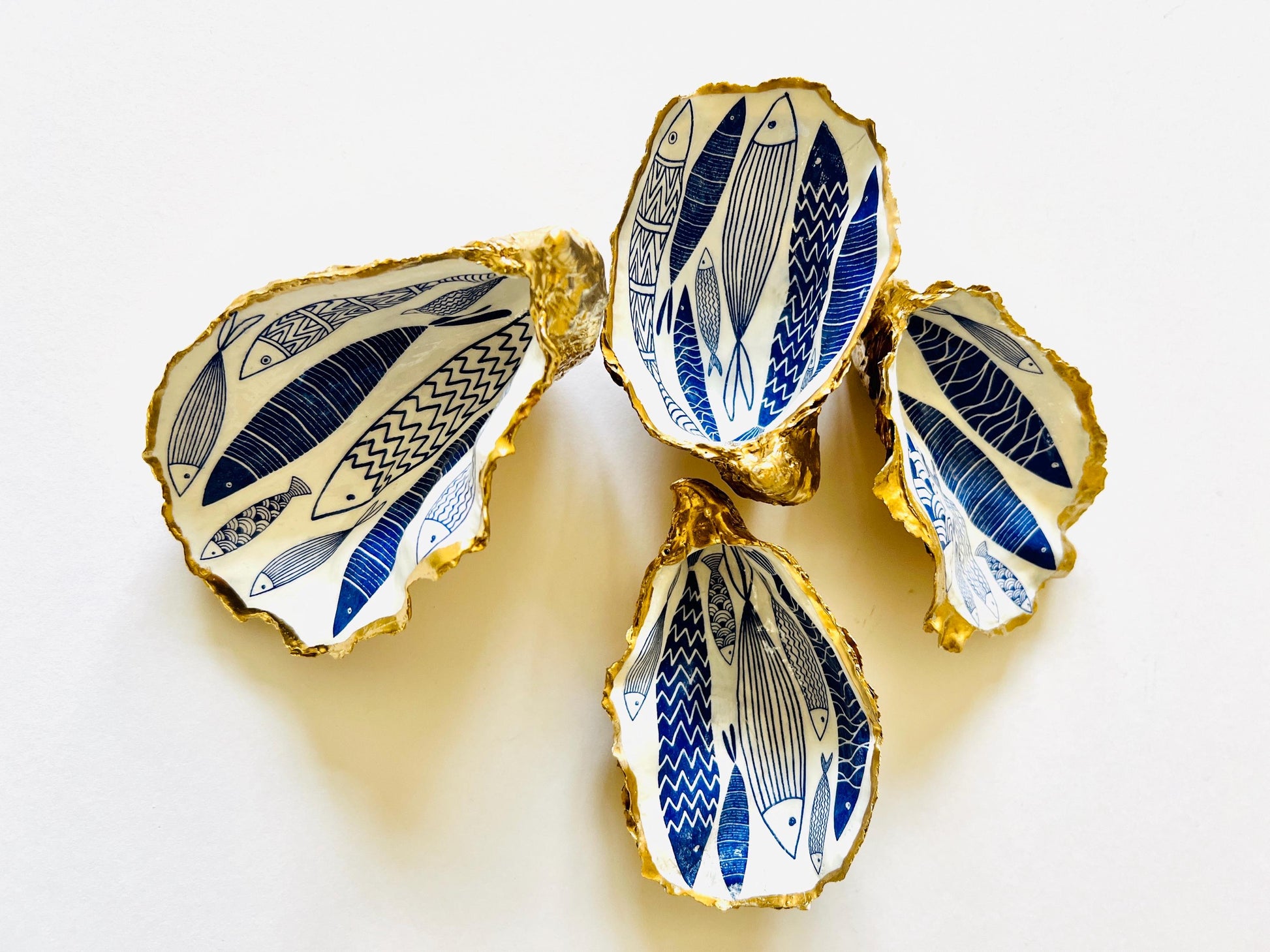 Luxury hand gilded Dorset oyster shell trinket dish featuring a refined blue fish motif, edged in liquid gold leaf and sealed in crystal clear resin. Sustainable coastal ring holder handmade by the artist in Surrey and presented in eco friendly branded gift packaging. Elegant beach house decor piece ideal for jewellery storage, wedding styling or sophisticated coastal interiors.