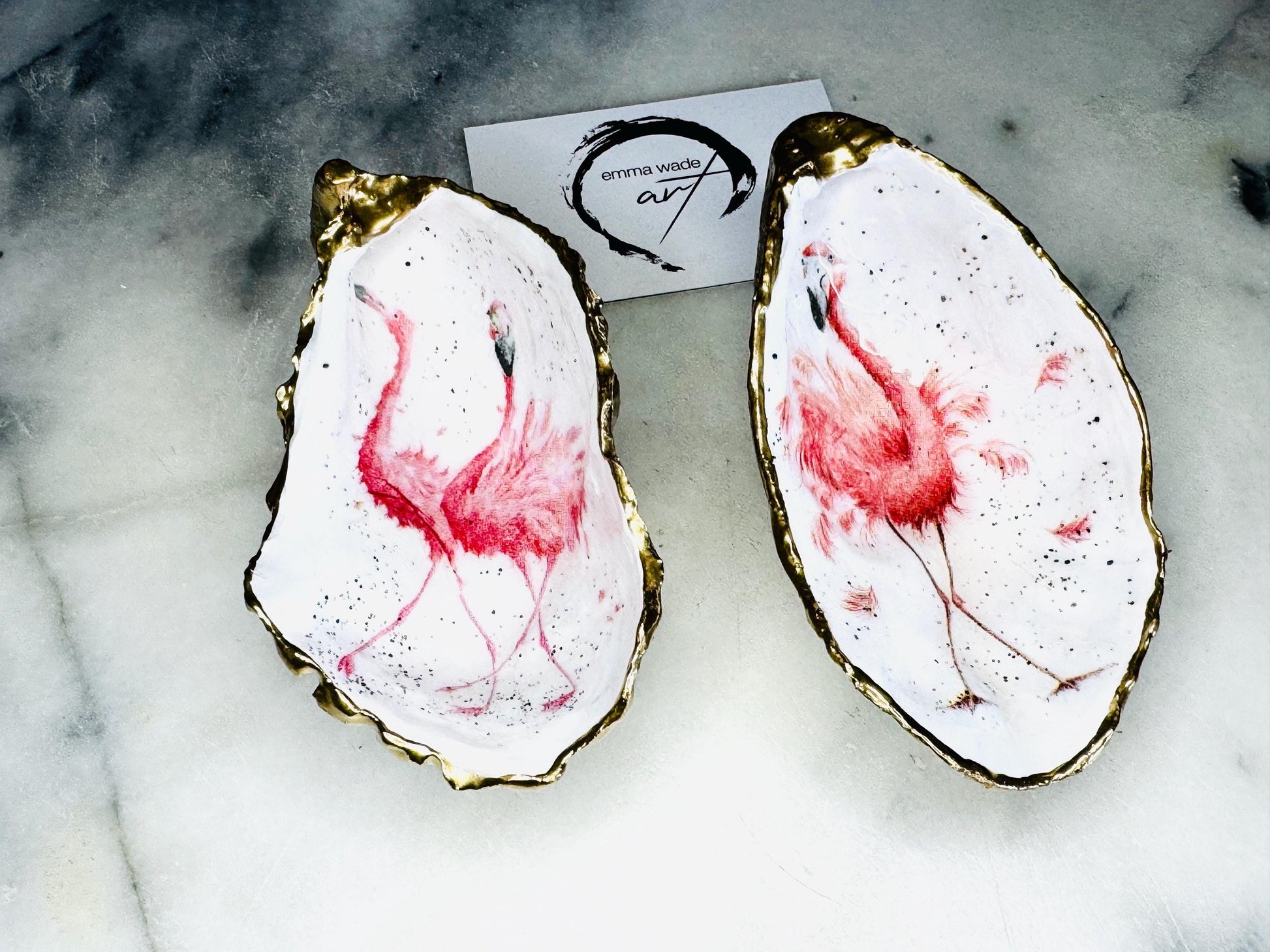 Handmade Dorset oyster shell trinket dishes featuring elegant pink flamingo bird artwork with hand-painted gold leaf edging and glossy crystal clear resin. Coastal flamingo jewellery holders styled on a white marble background with tropical blush pink tones and luxury coastal home décor styling.