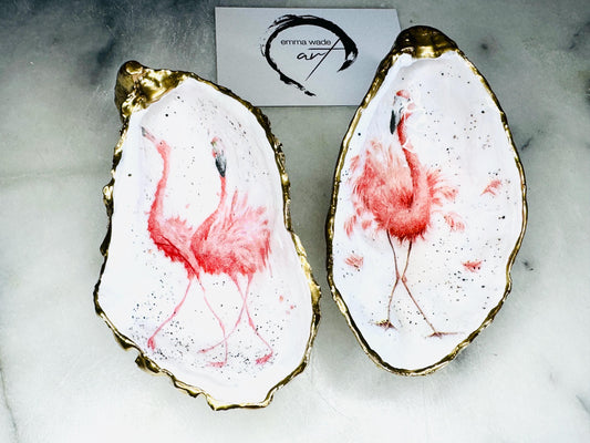Handmade Dorset oyster shell trinket dishes featuring elegant pink flamingo bird artwork with hand-painted gold leaf edging and glossy crystal clear resin. Coastal flamingo jewellery holders styled on a white marble background with tropical blush pink tones and luxury coastal home décor styling.