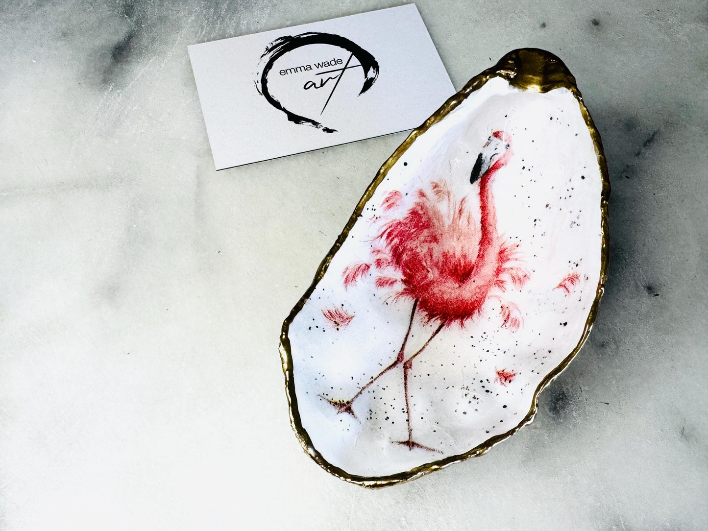 Handmade Dorset oyster shell trinket dishes featuring elegant pink flamingo bird artwork with hand-painted gold leaf edging and glossy crystal clear resin. Coastal flamingo jewellery holders styled on a white marble background with tropical blush pink tones and luxury coastal home décor styling.