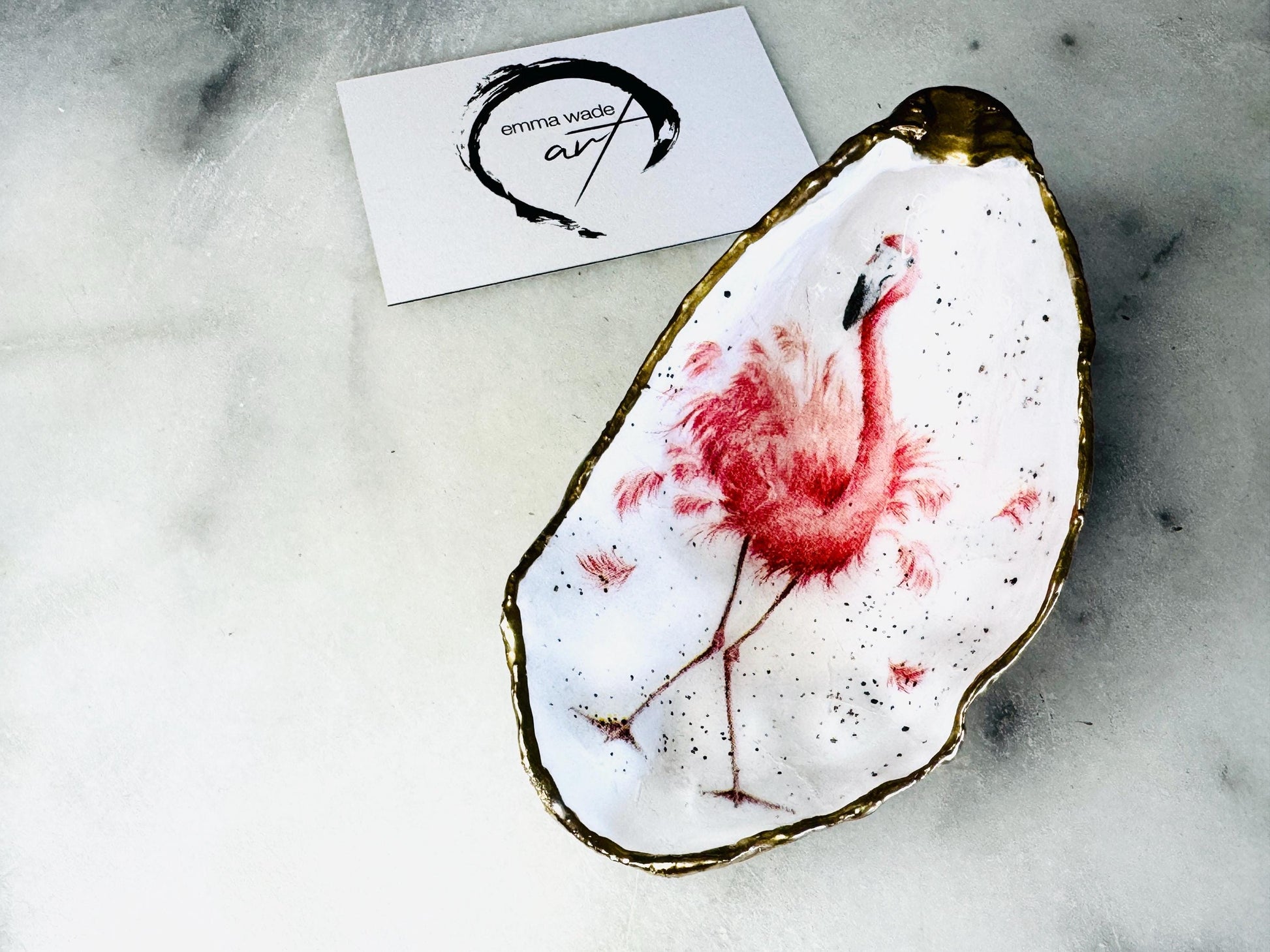 Handmade Dorset oyster shell trinket dishes featuring elegant pink flamingo bird artwork with hand-painted gold leaf edging and glossy crystal clear resin. Coastal flamingo jewellery holders styled on a white marble background with tropical blush pink tones and luxury coastal home décor styling.