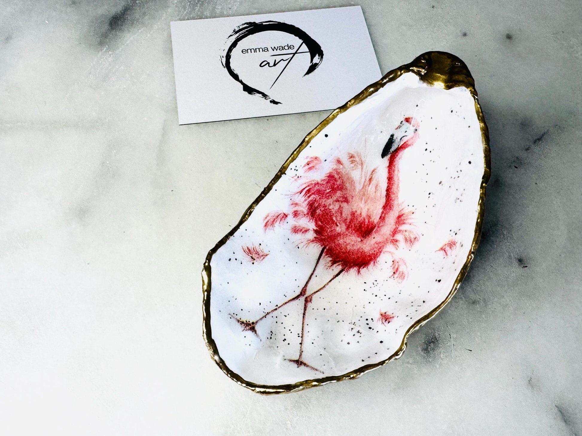 Handmade Dorset oyster shell trinket dishes featuring elegant pink flamingo bird artwork with hand-painted gold leaf edging and glossy crystal clear resin. Coastal flamingo jewellery holders styled on a white marble background with tropical blush pink tones and luxury coastal home décor styling.