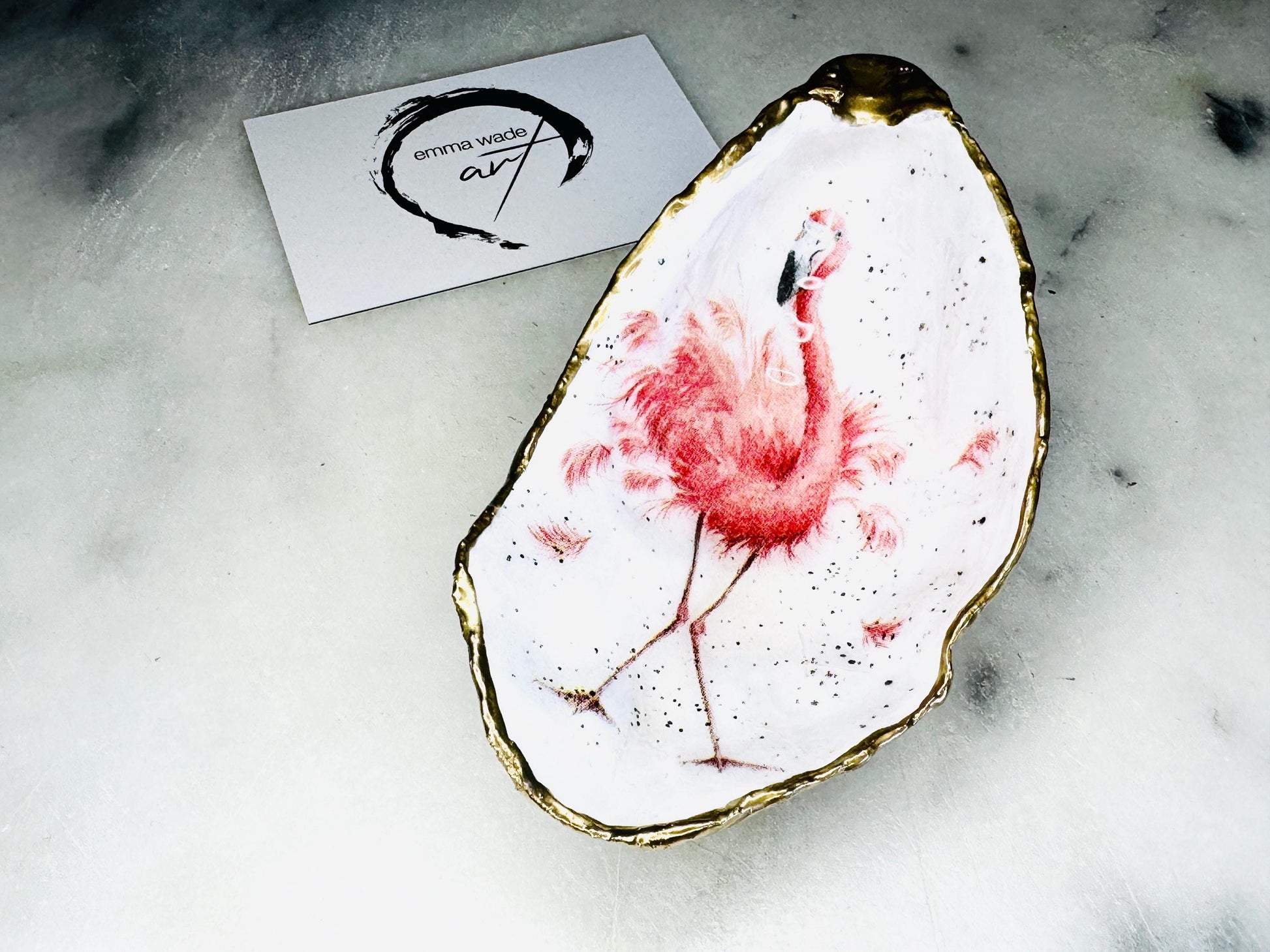 Handmade Dorset oyster shell trinket dishes featuring elegant pink flamingo bird artwork with hand-painted gold leaf edging and glossy crystal clear resin. Coastal flamingo jewellery holders styled on a white marble background with tropical blush pink tones and luxury coastal home décor styling.