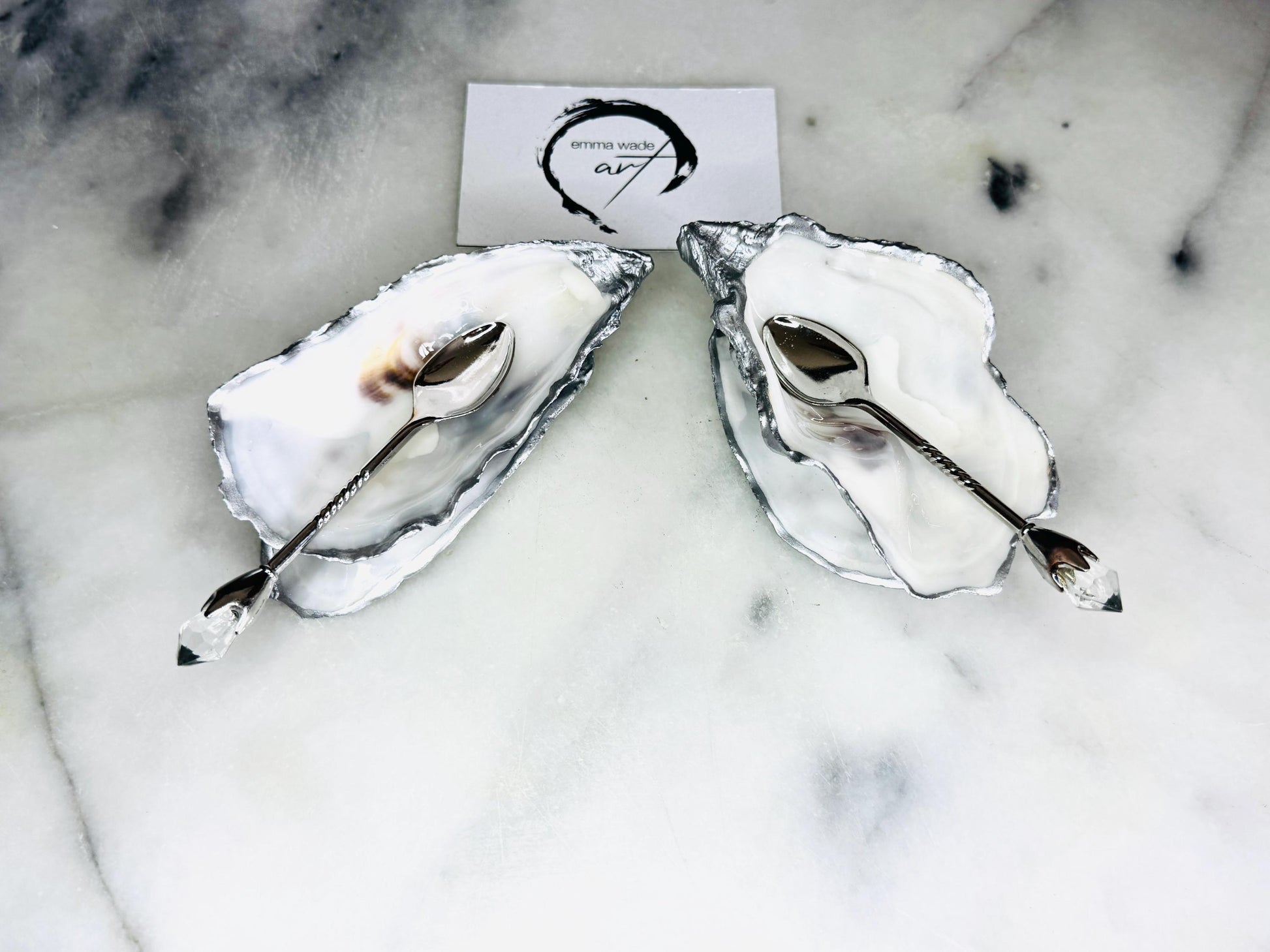 Handmade pearl oyster shell salt and pepper pinch pots with silver leaf accents and optional crystal spoons. Coastal tableware set made from natural Dorset oyster shells, polished to a natural white pearl finish and sealed with food-safe glossy resin. Elegant shell salt dishes photographed on a light background, showing two domed shells with matching bases, ideal for serving salt, pepper or spices at stylish dinner tables and special occasions.